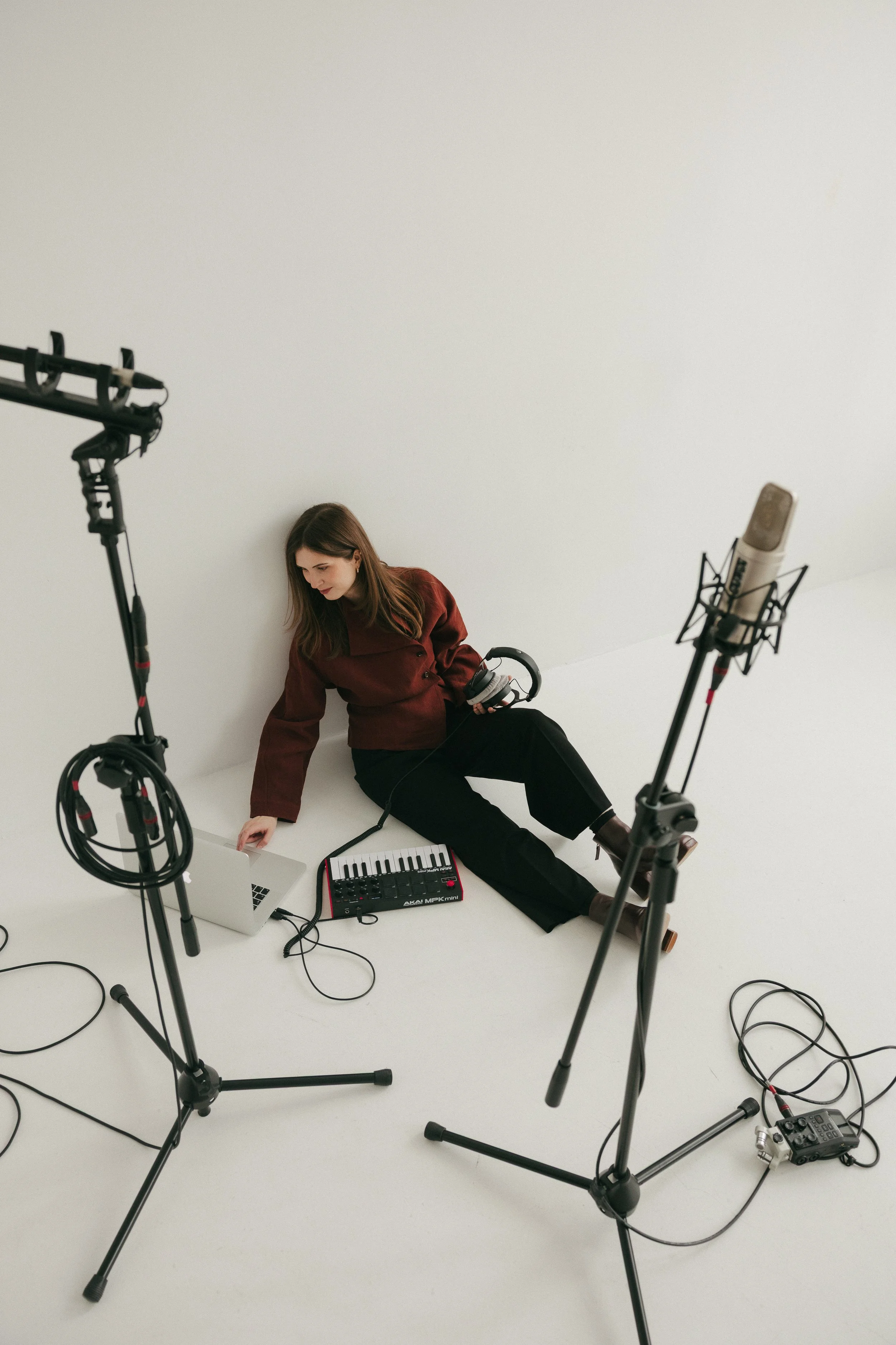 Woman in a red jacket sitting on the floor in a photography studio, surrounded by professional lighting equipment, a keyboard, and a laptop.