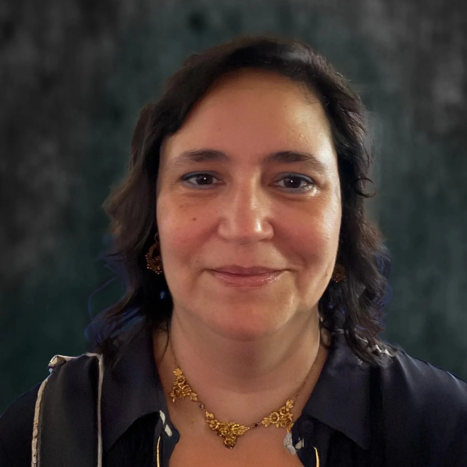 Close-up of a woman with shoulder-length dark hair, wearing jewelry and a black top. She is smiling gently and looking at the camera.