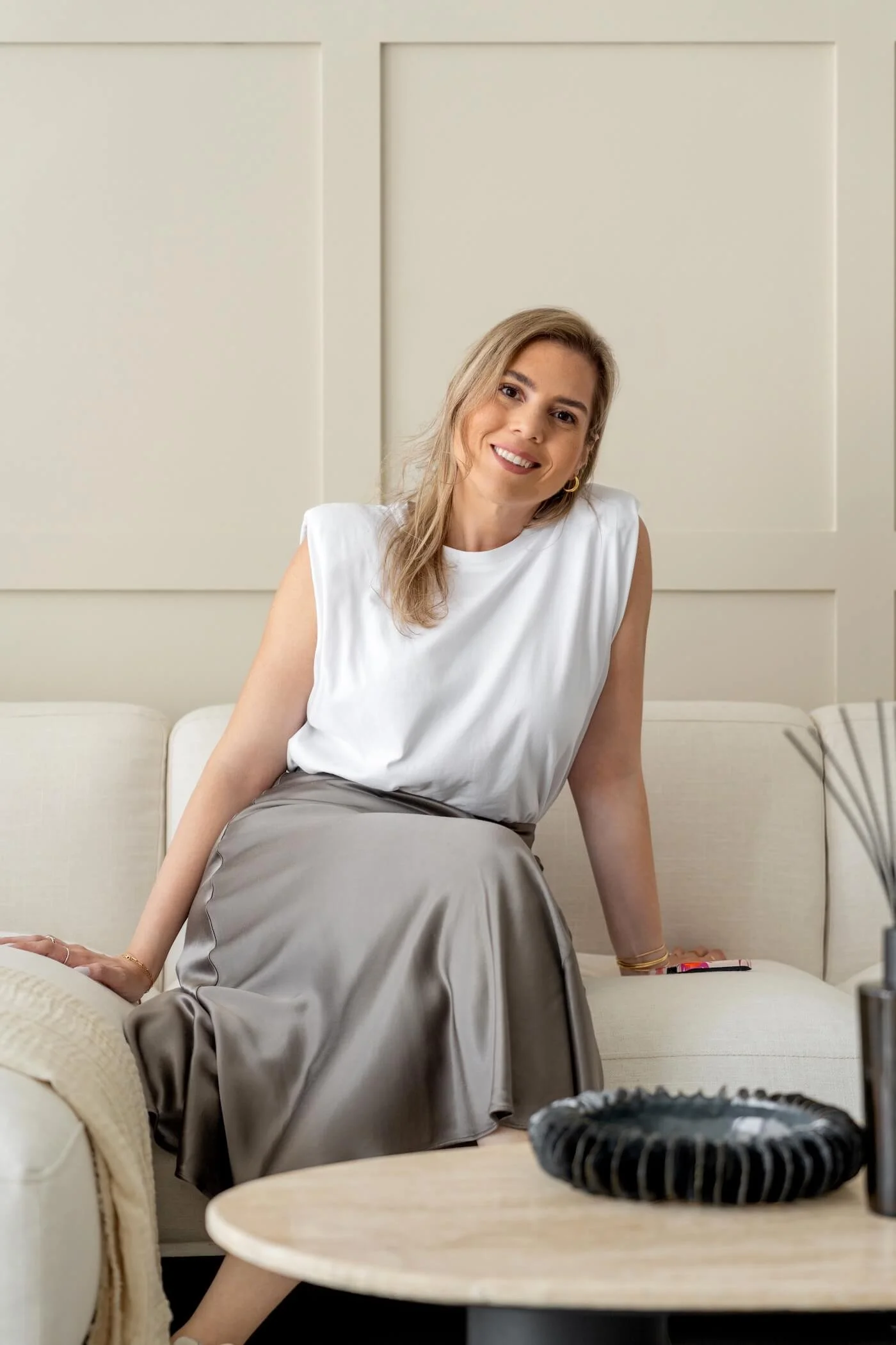 The founder of the interior design studio sitting on a beige sofa, in a modern room with neutral-colored walls.