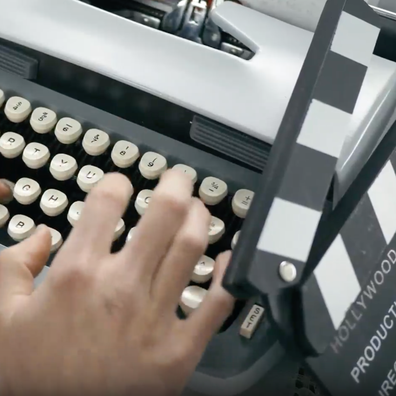 Une main sur une machine à écrire rédige un scénario, un clap de cinéma est placé sur le coté de ma machine