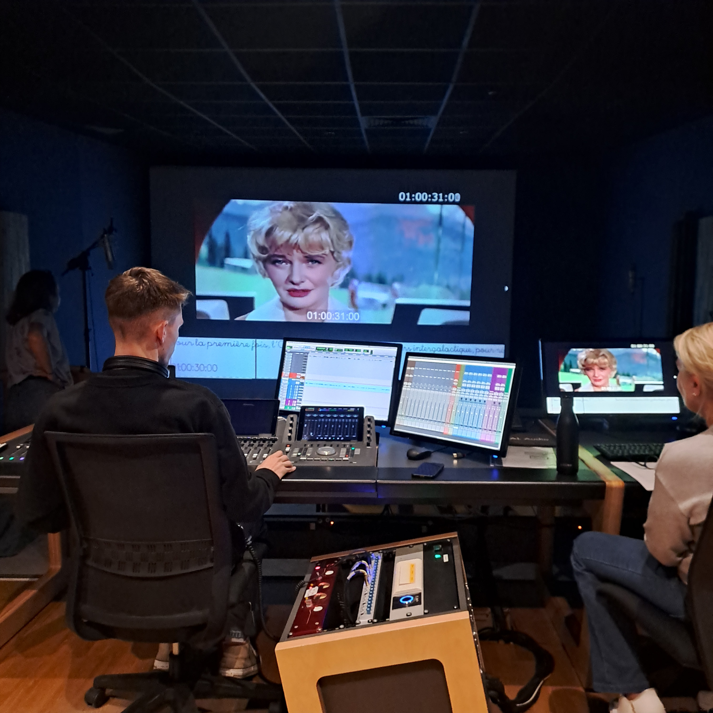 Deux personnes sont dans une cabine de doublage et interagissent sur une console