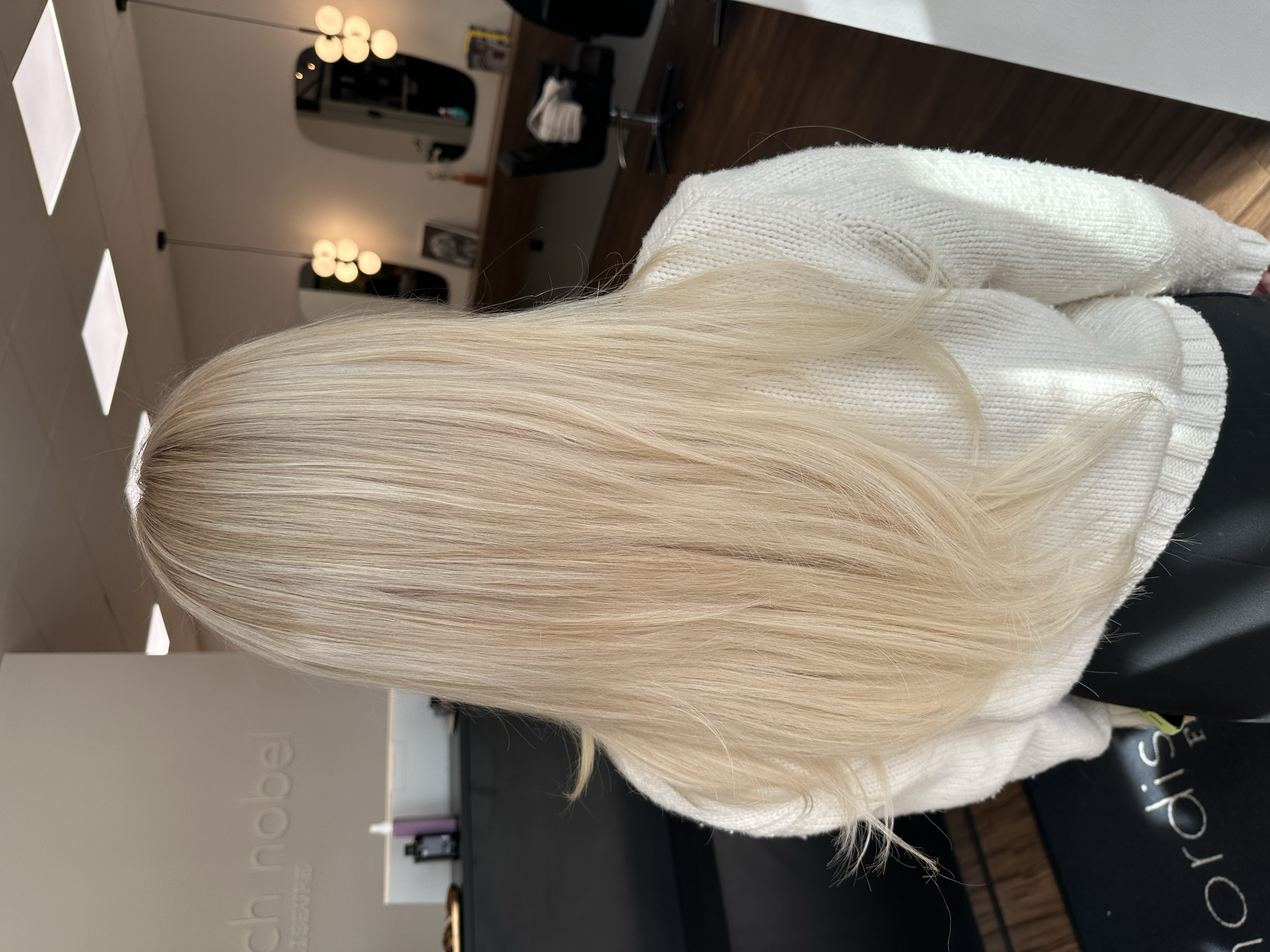 Frau mit langen, glatten, blonden Haaren sitzt in einem Friseursalon. Ergebnis einer Laurea Extensions Echthaarverlängerung.