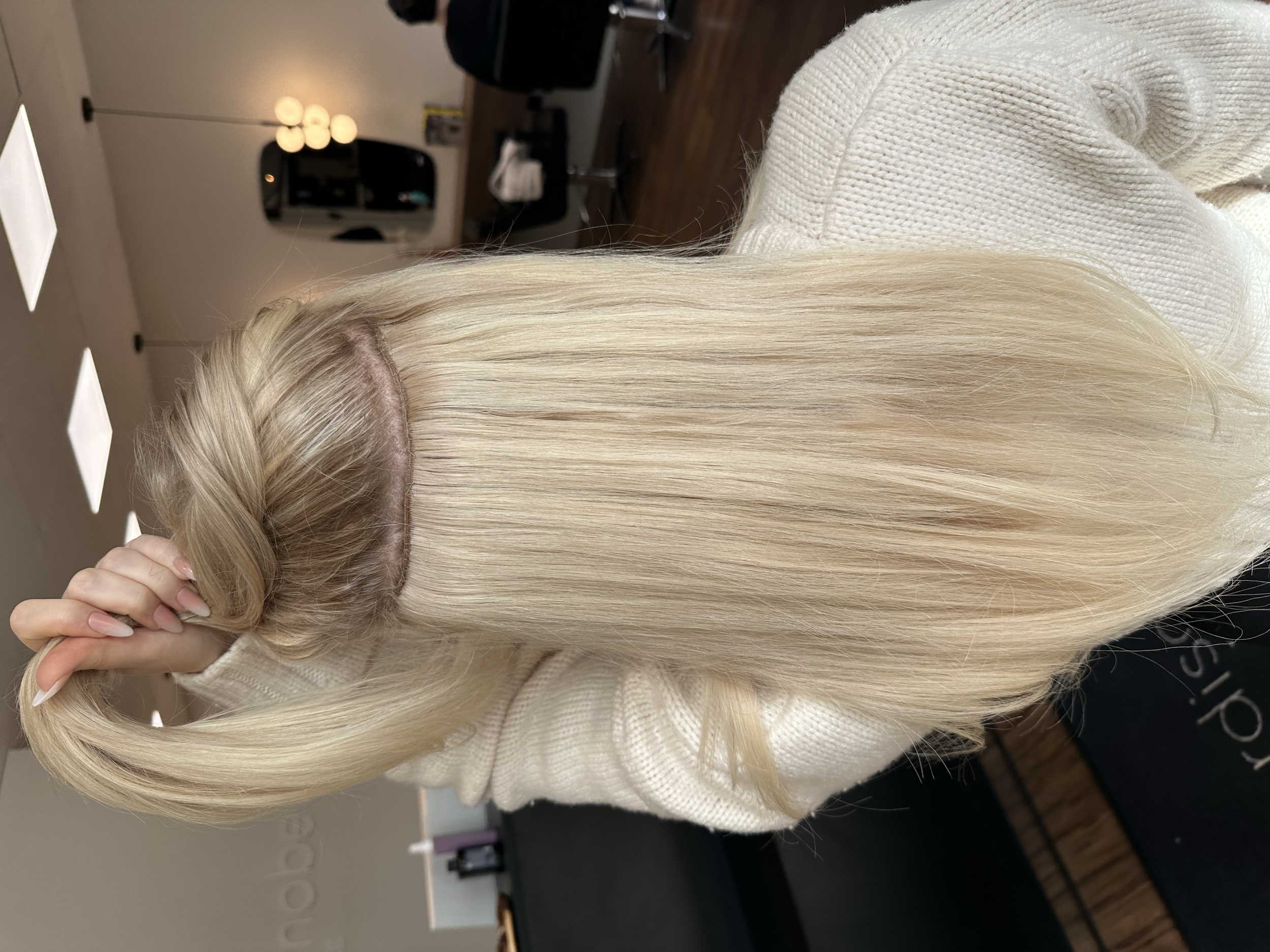 Nahe Blick auf das lange, glatte, blonde Haar einer Frau, die Laurea Extensions in der Hand hält.