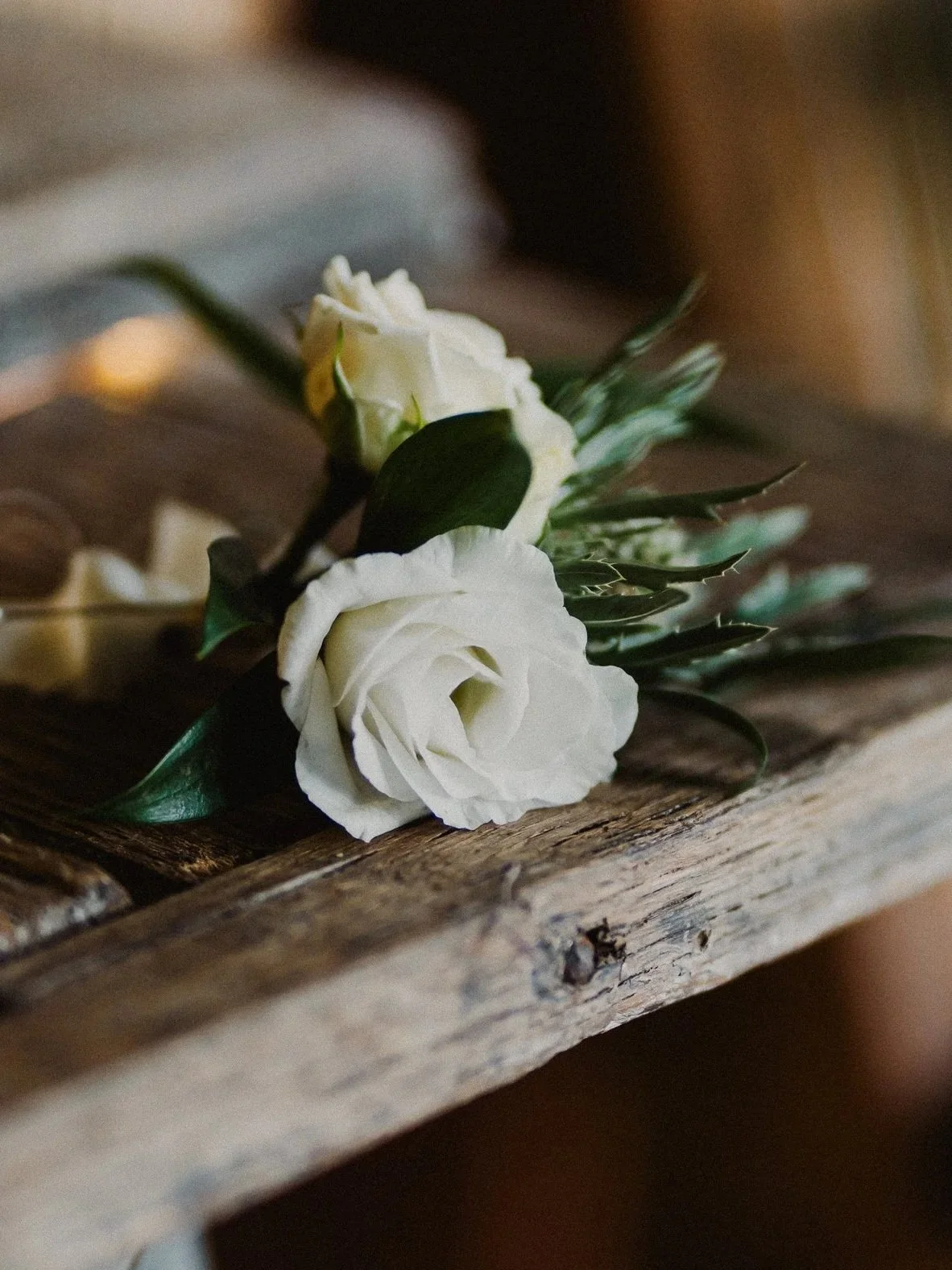 A white rose boutonniere with green leaves lying on a wooden surface.