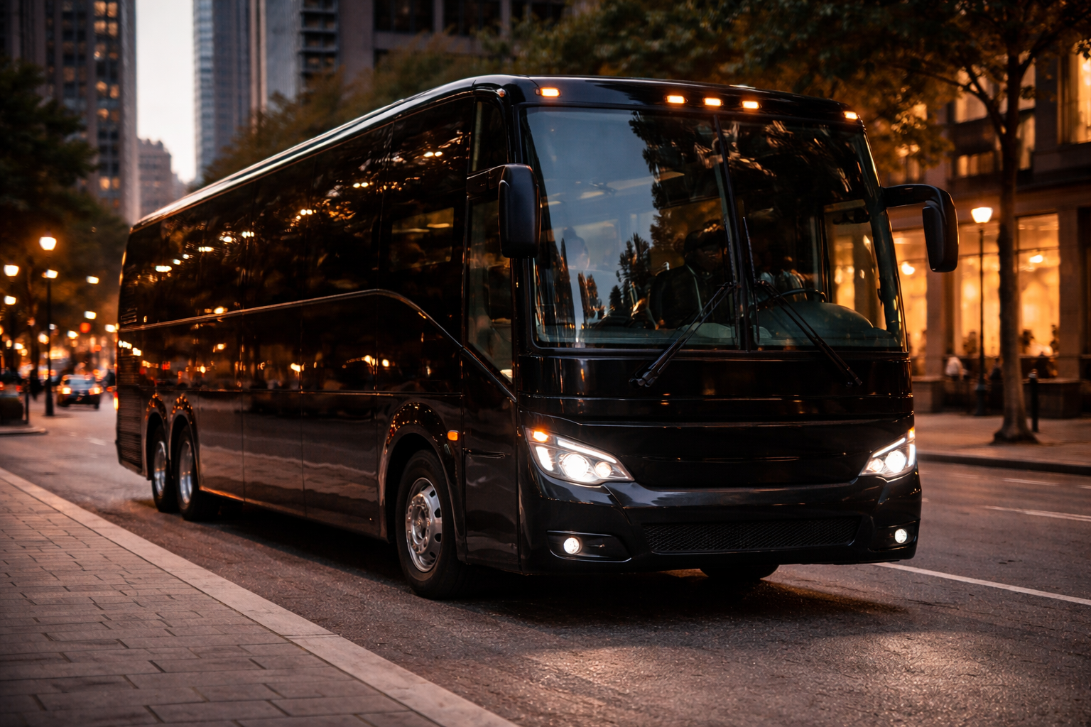 A black bus parked on a city street during dusk, with tall buildings and trees in the background.