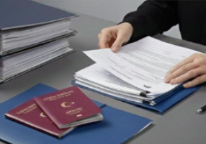 Person handling a large pile of documents and papers on a desk with two passports and a folder.
