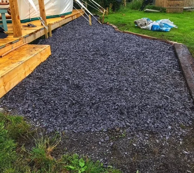 Freshly laid black gravel on a garden pathway beside a wooden deck in a backyard.