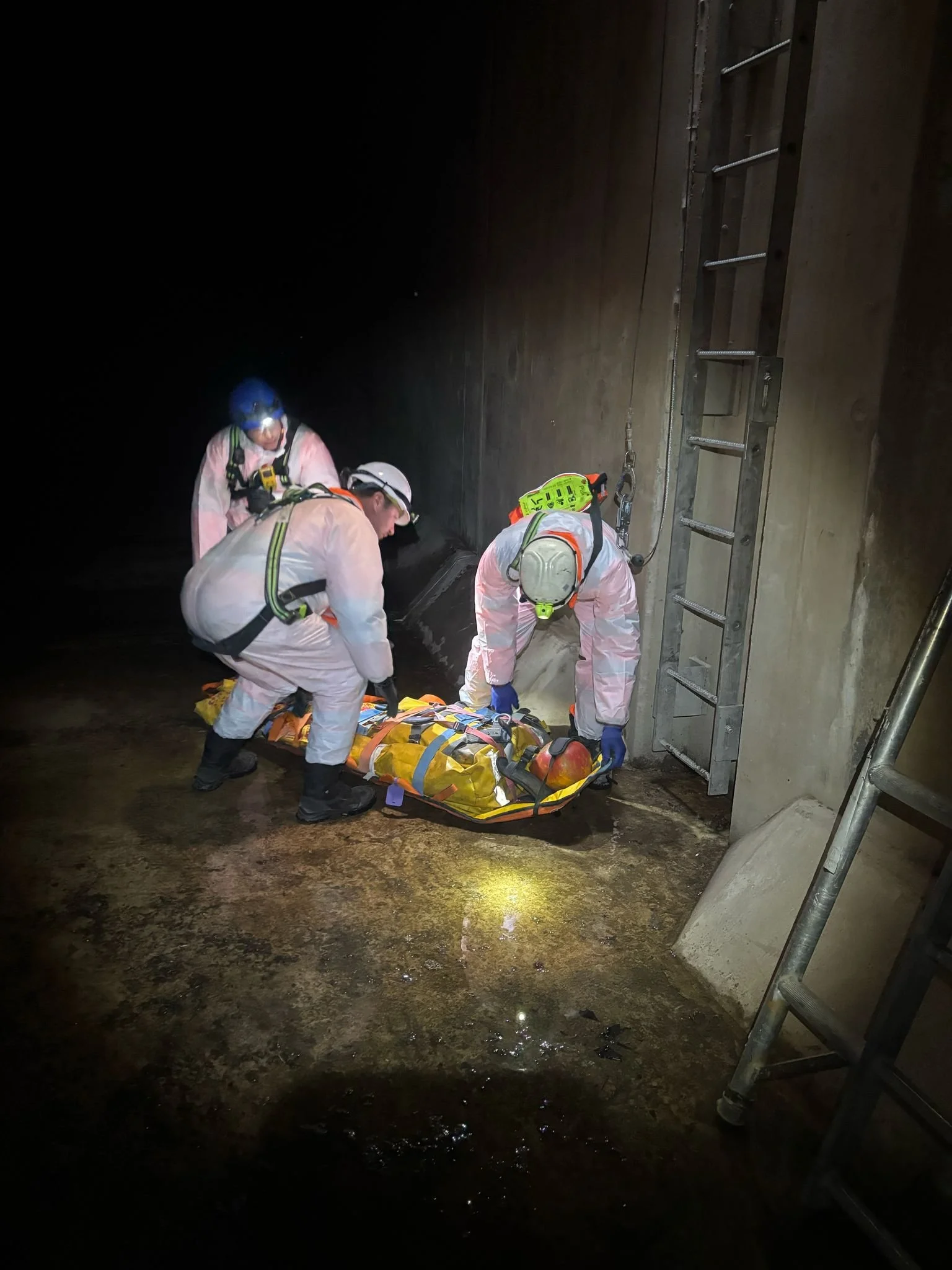 Emergency responders in protective gear are lifting a person on a stretcher inside a dark underground tunnel.