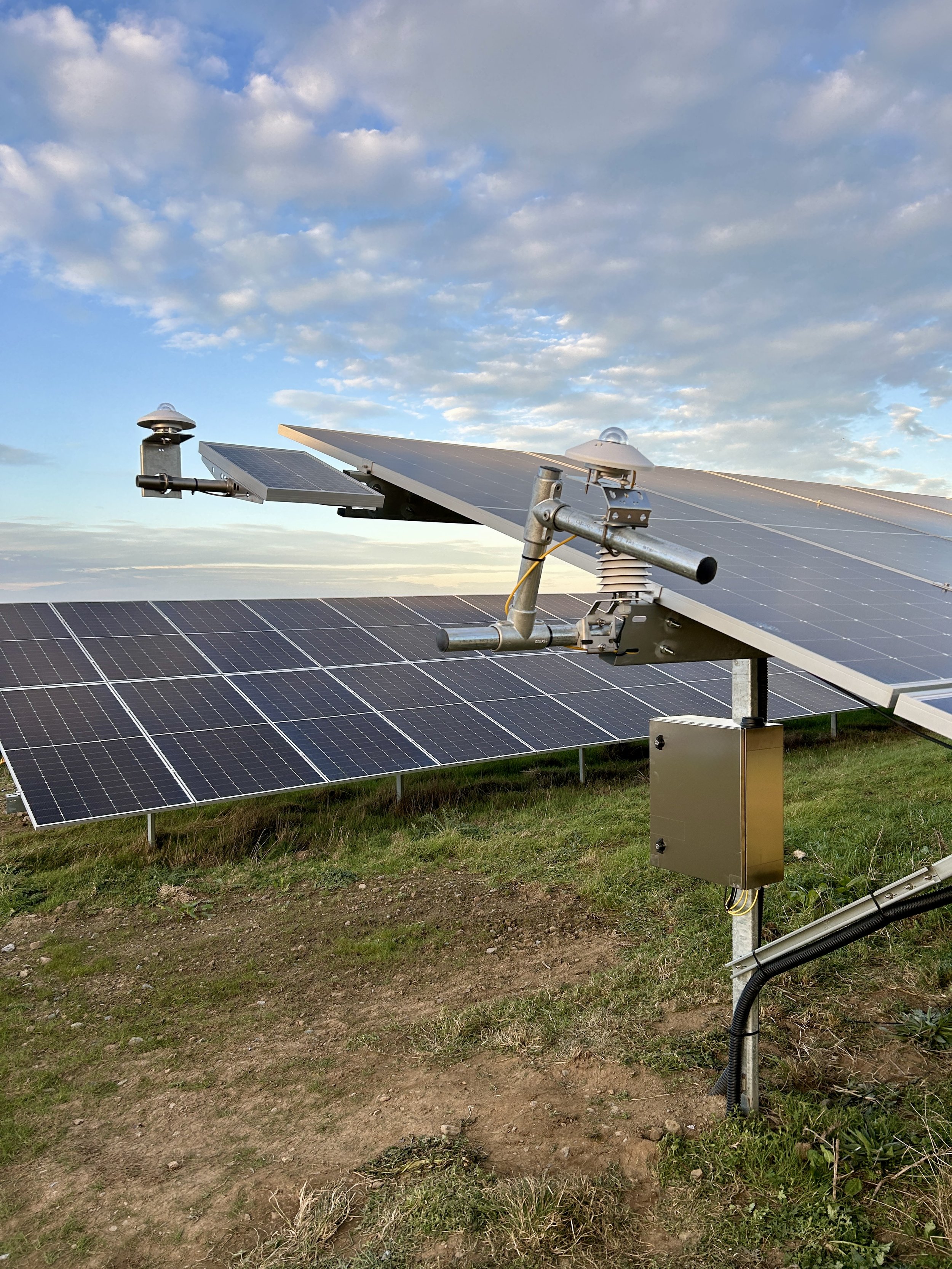 Solar panels on a grassy field under a blue sky with scattered clouds.
