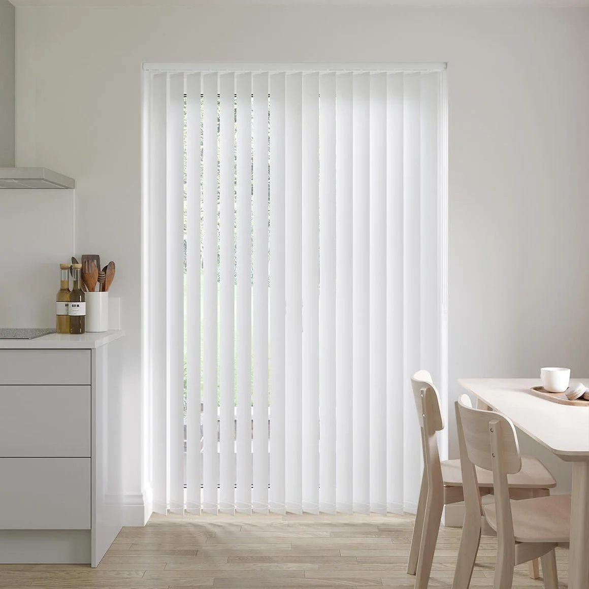 Modern kitchen with white vertical blinds in front of a glass door, light wood flooring, and minimalistic furniture.