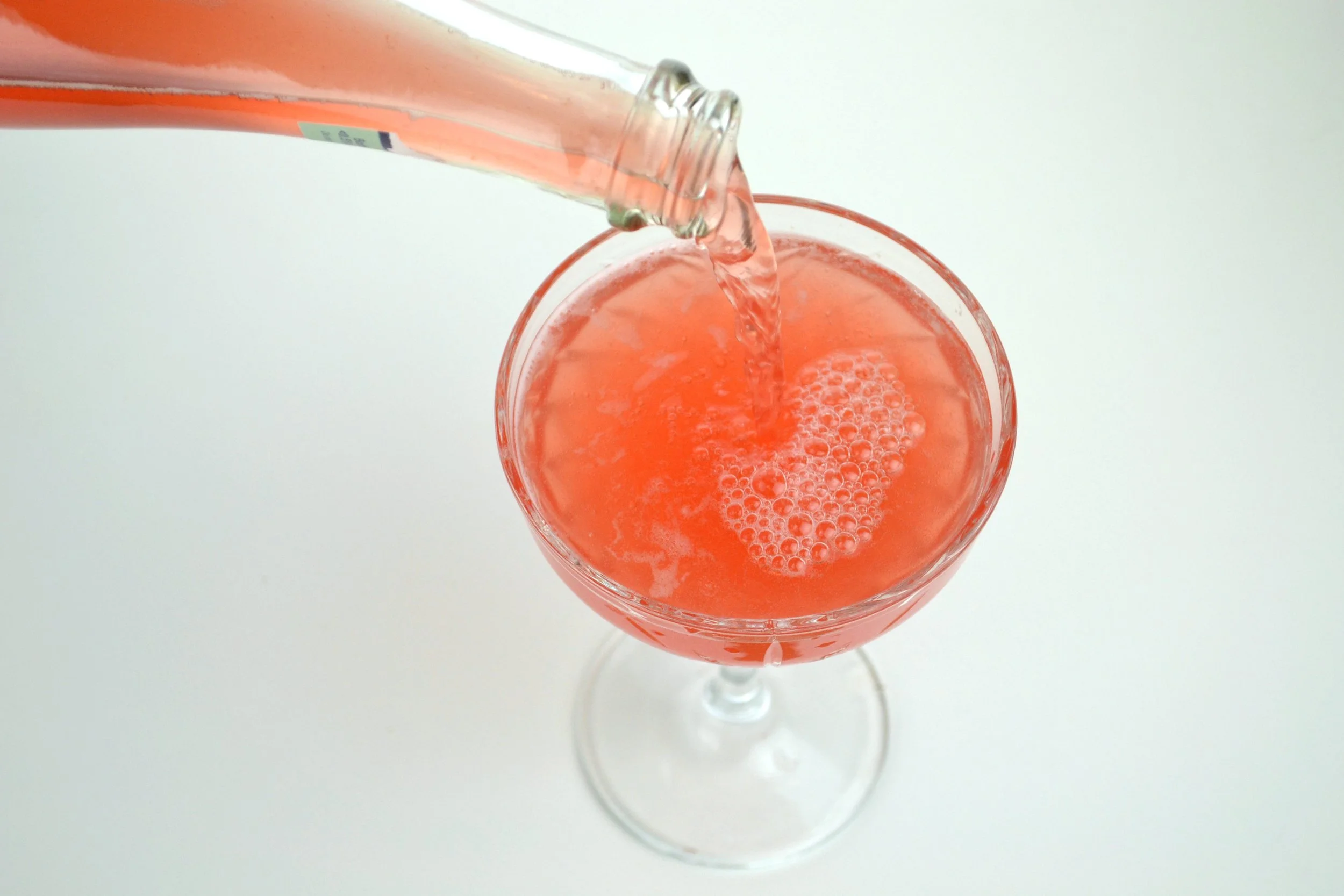 A glass of pink kombucha being poured from a bottle against a white background.