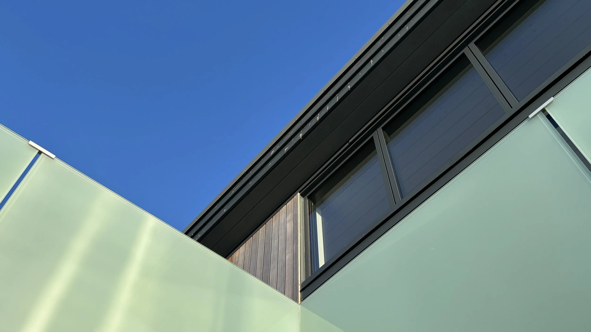 Close-up of modern building with black and green exterior panels and large windows under a clear blue sky.