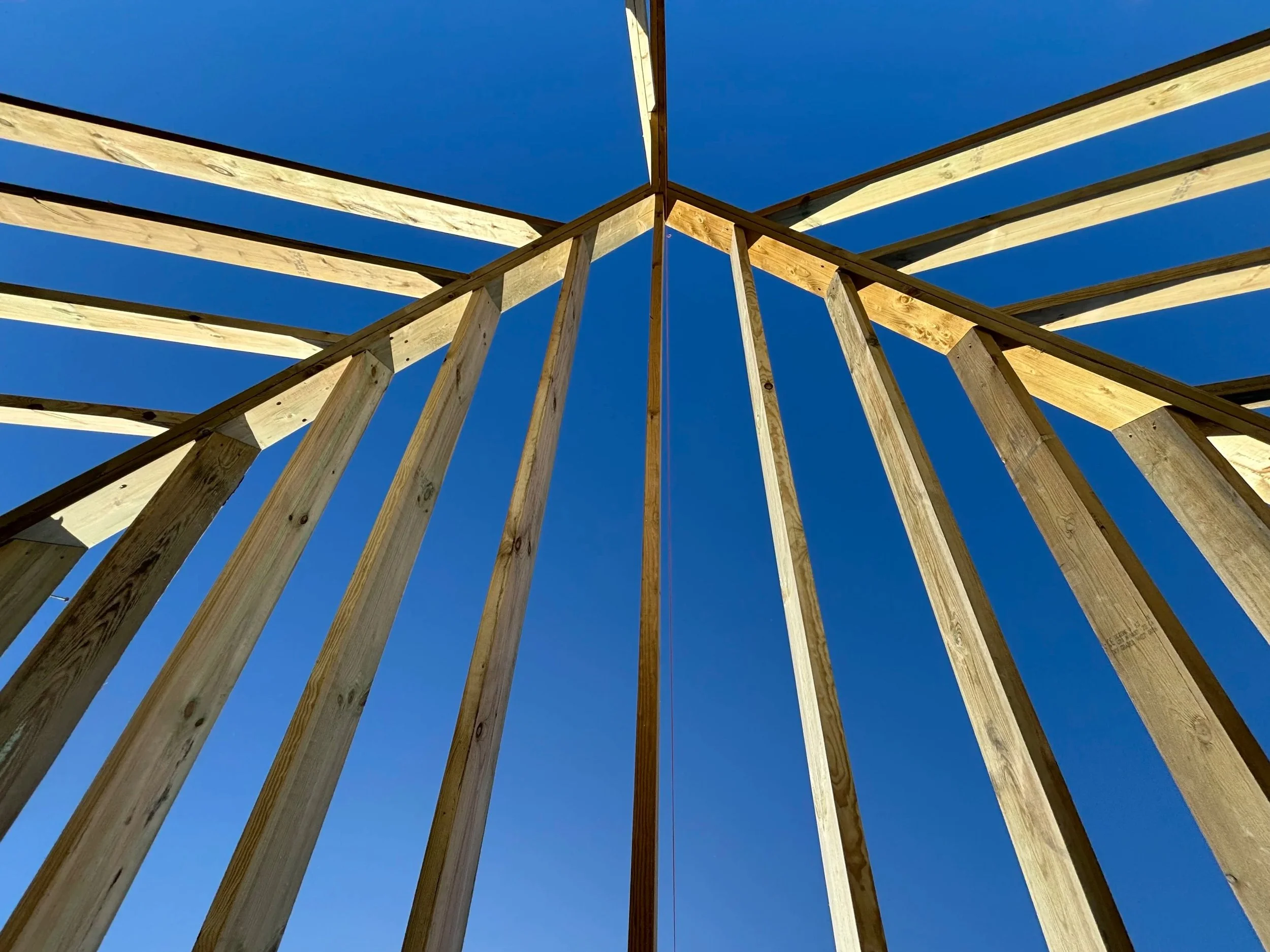 Looking up at a wooden structure frame against a clear blue sky.