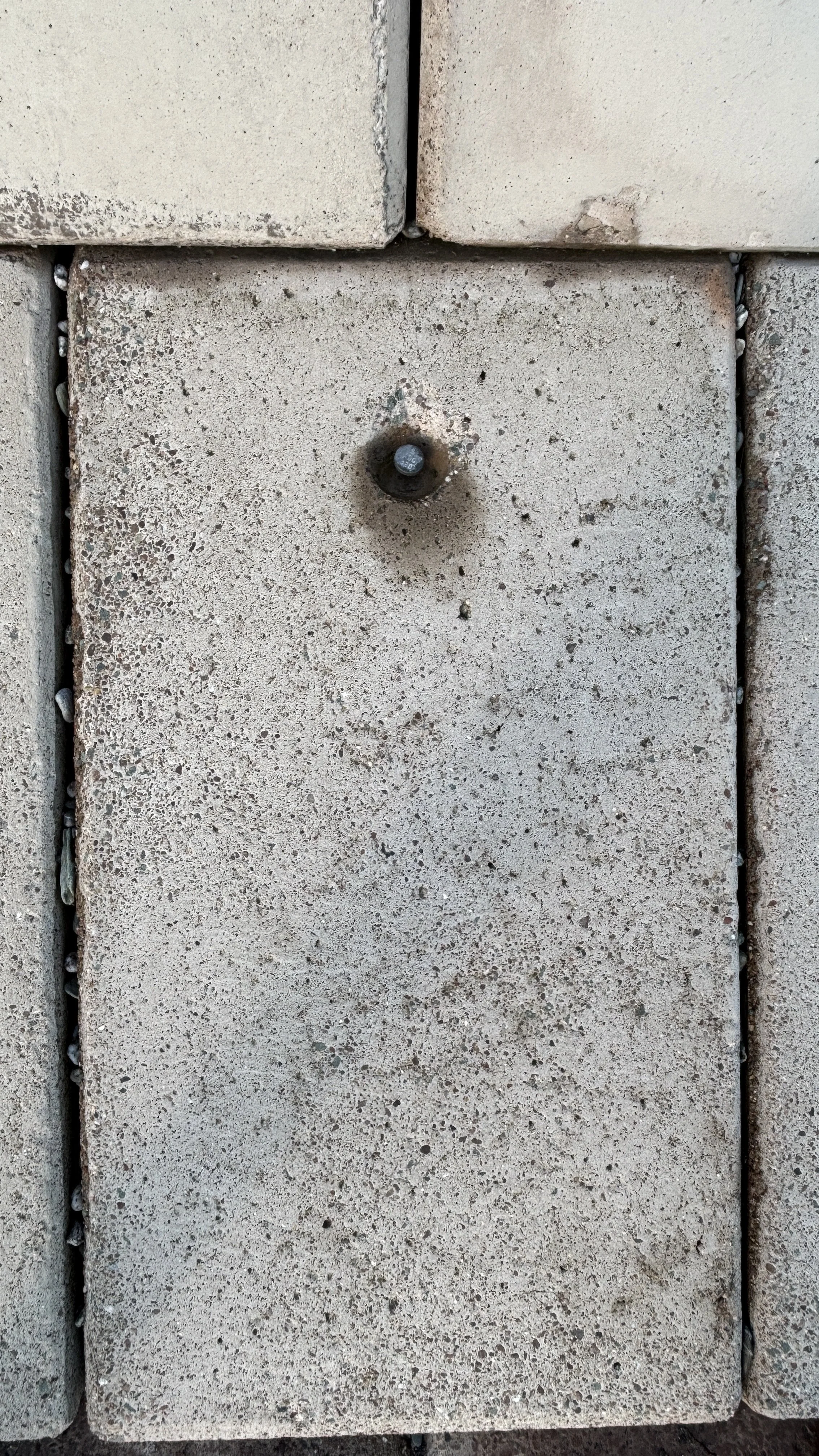 Close-up of a concrete brick wall with one brick missing, revealing a bolt in the center.