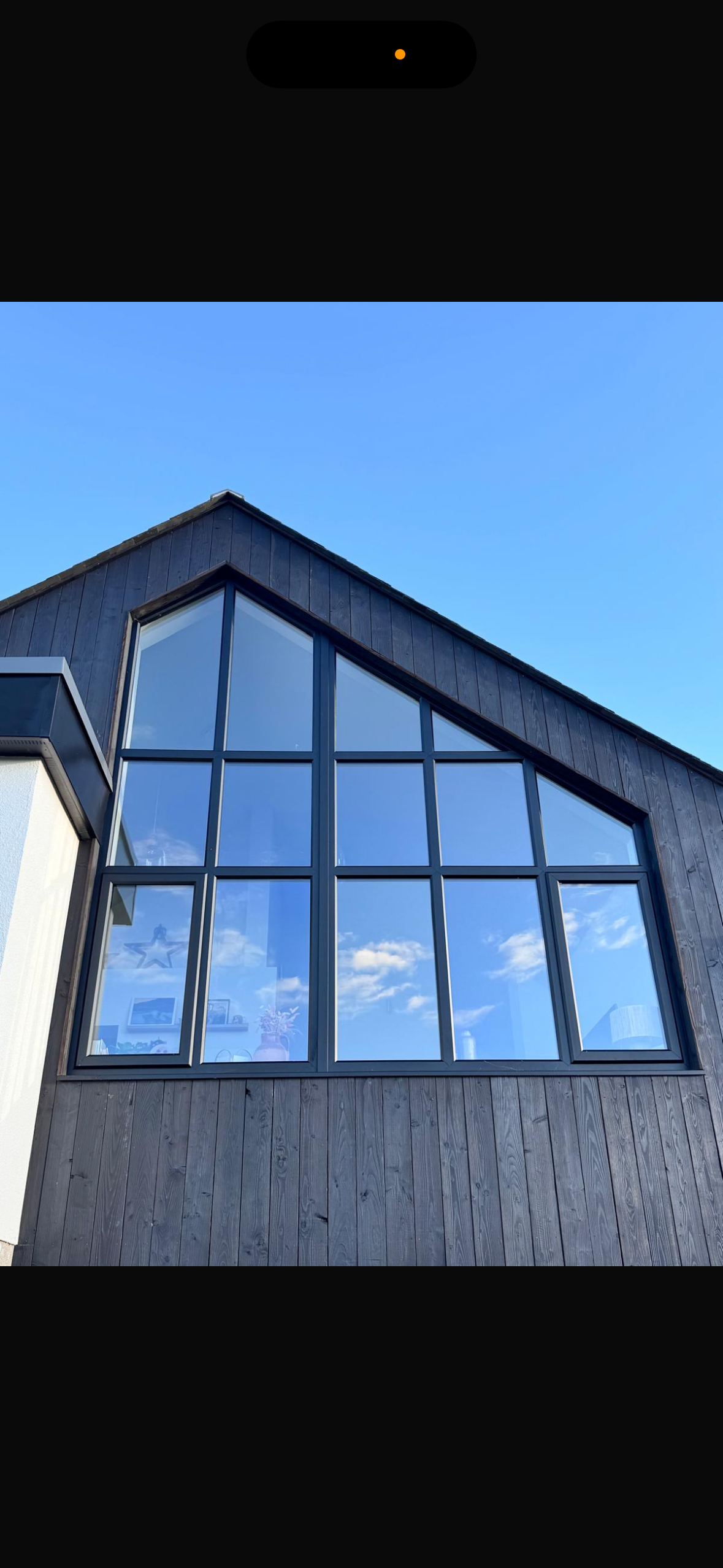 Modern house with large, multi-pane windows reflecting a blue sky with some clouds.