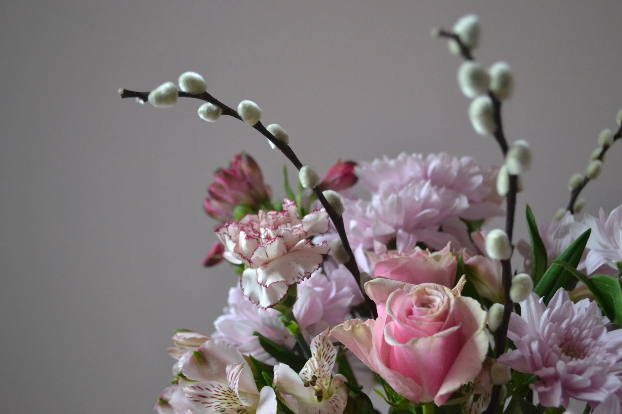 Close-up of a bouquet of pink and white flowers with pussy willow branches against a neutral background.