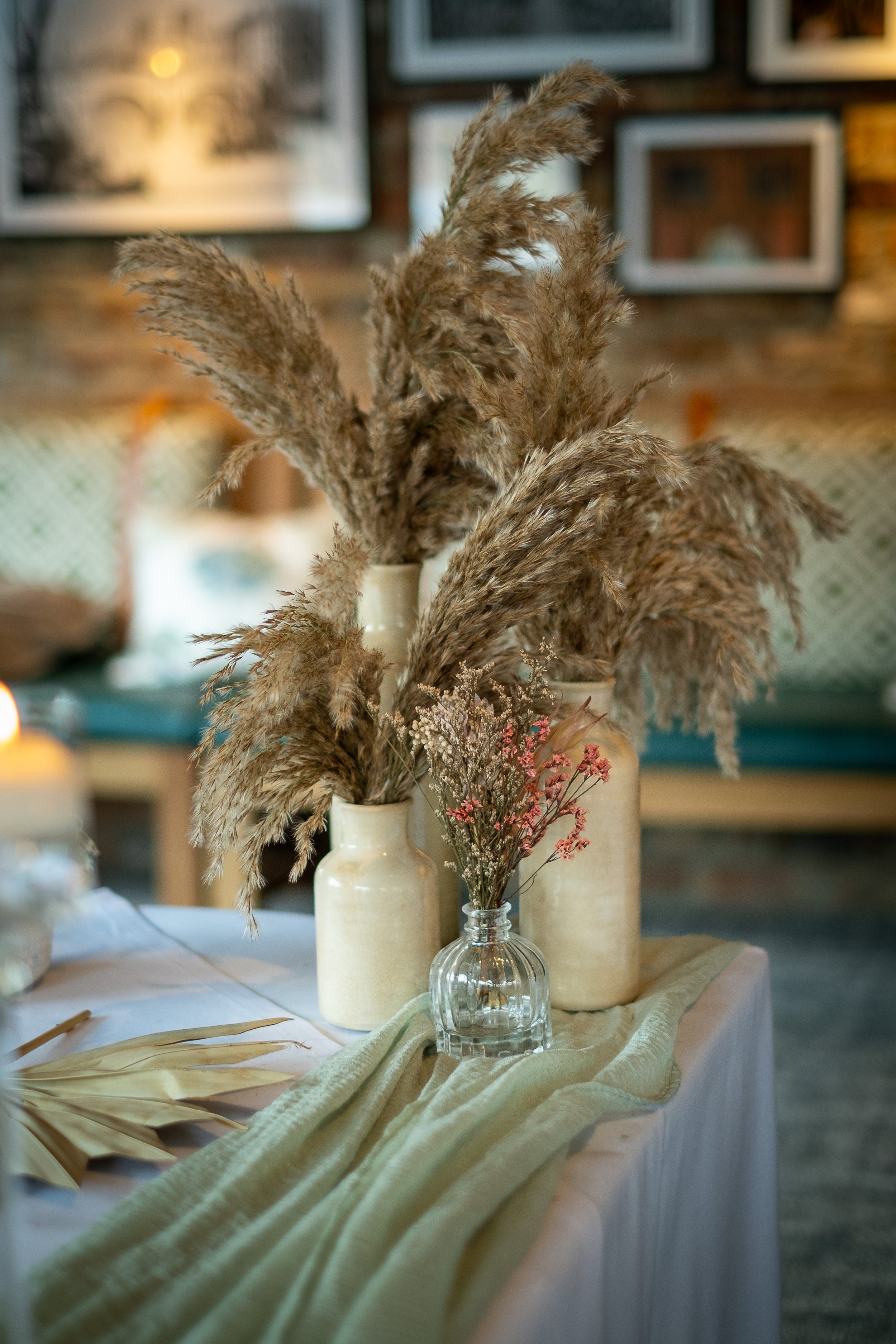 Decorative dried pampas grass and small dried flowers in vases on a table with a cream-colored tablecloth.