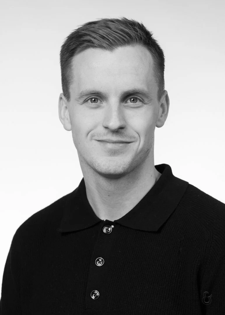 Black and white headshot of a smiling man in a polo shirt, looking directly at the camera against a plain background.