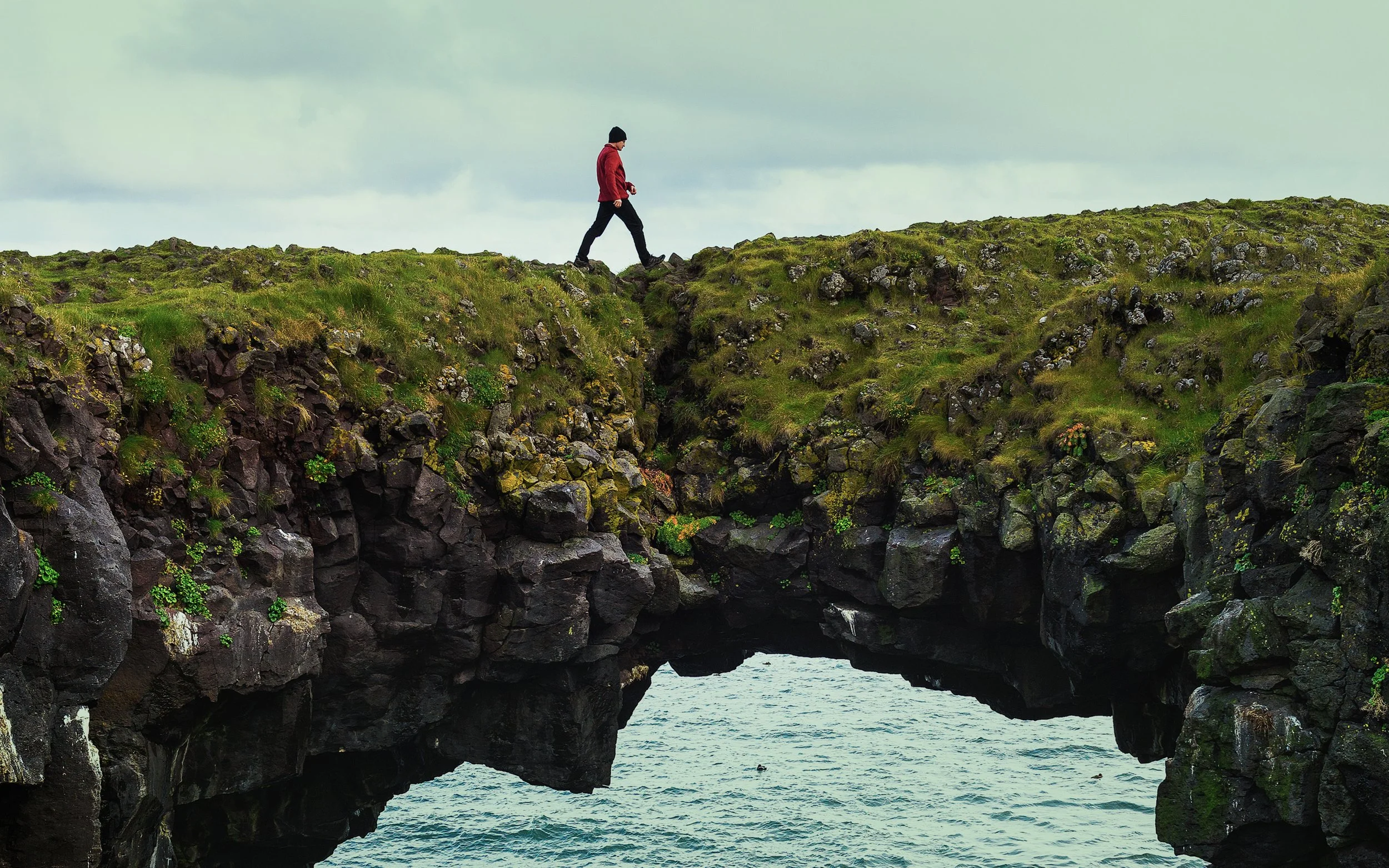 Einstaklingur gengur yfir klettabrú í íslensku landslagi – táknræn mynd fyrir persónulegan vöxt, áskoranir og framfarir í einstaklingsviðtölum hjá Sálfræðiklíníkinni.
