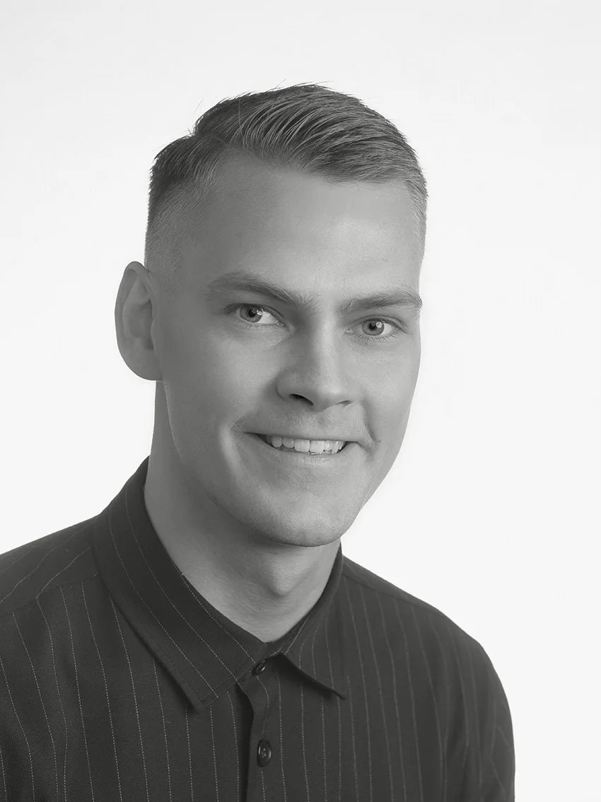 Black and white portrait of a young man with short, neat hair, smiling, wearing a dark pinstripe shirt, against a plain light background.
