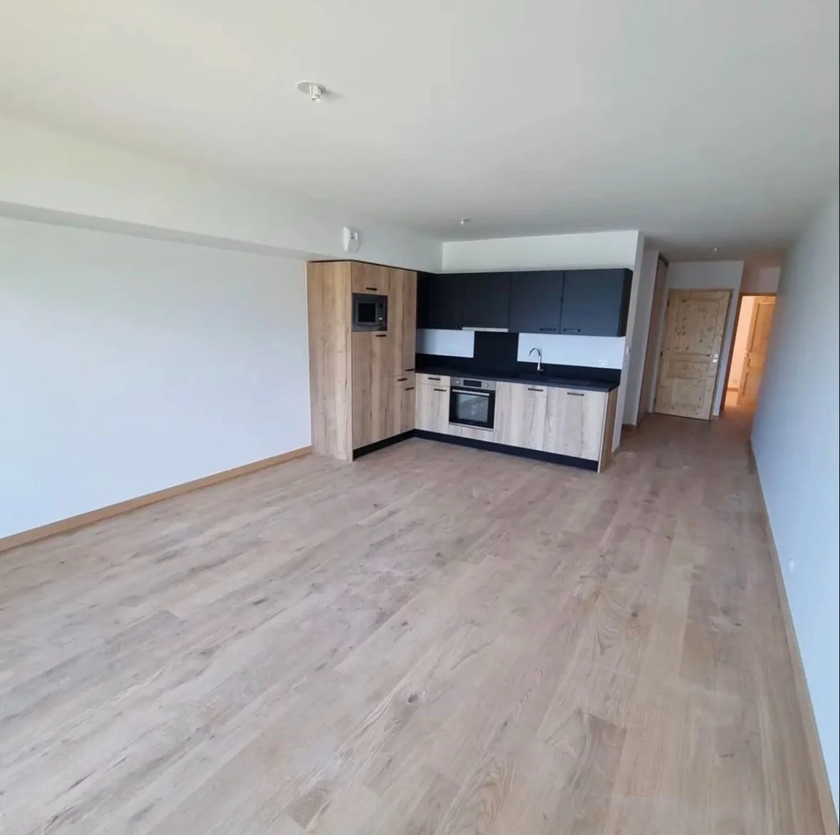 Salon avec cuisine ouverte en bois clair, meubles noirs, et électroménagers intégrés.