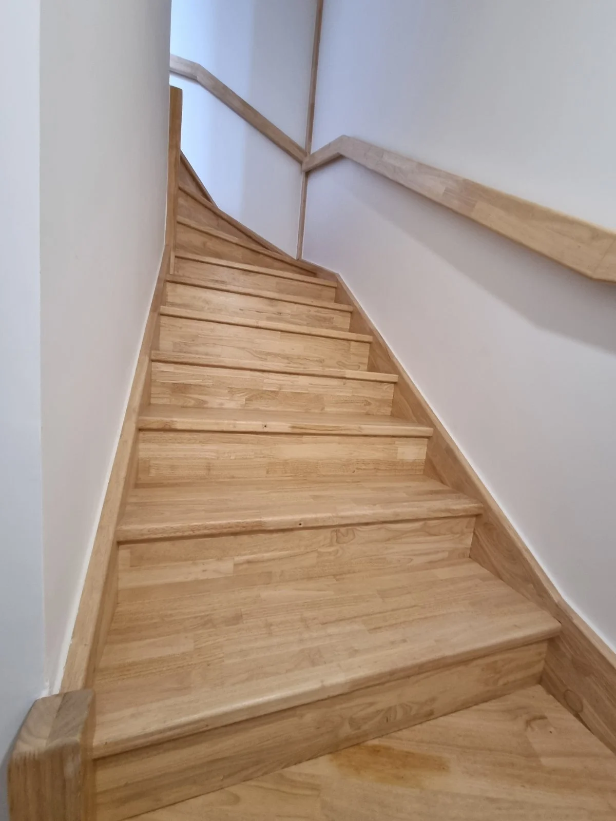 Escalier en bois clair avec rampe en bois dans un intérieur blanc.
