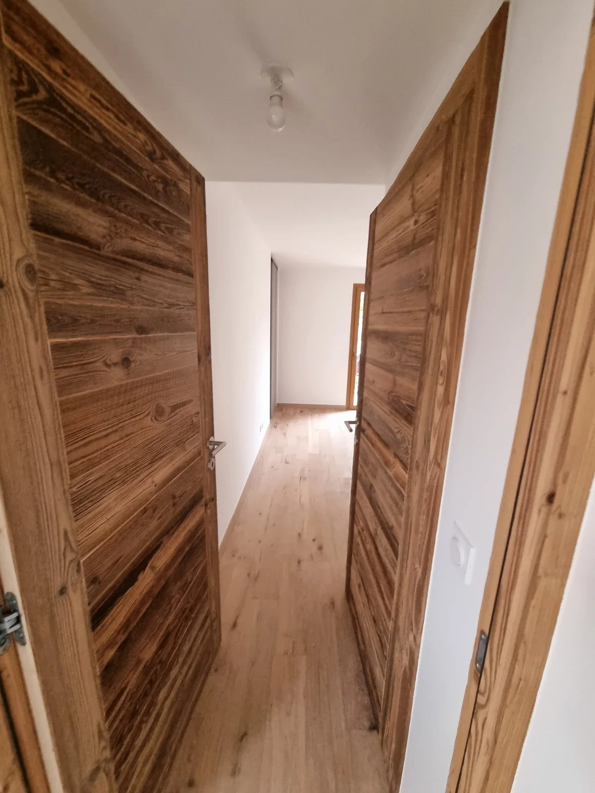 Photographie d'un couloir avec des portes en bois de chaque côté et un sol en bois clair.
