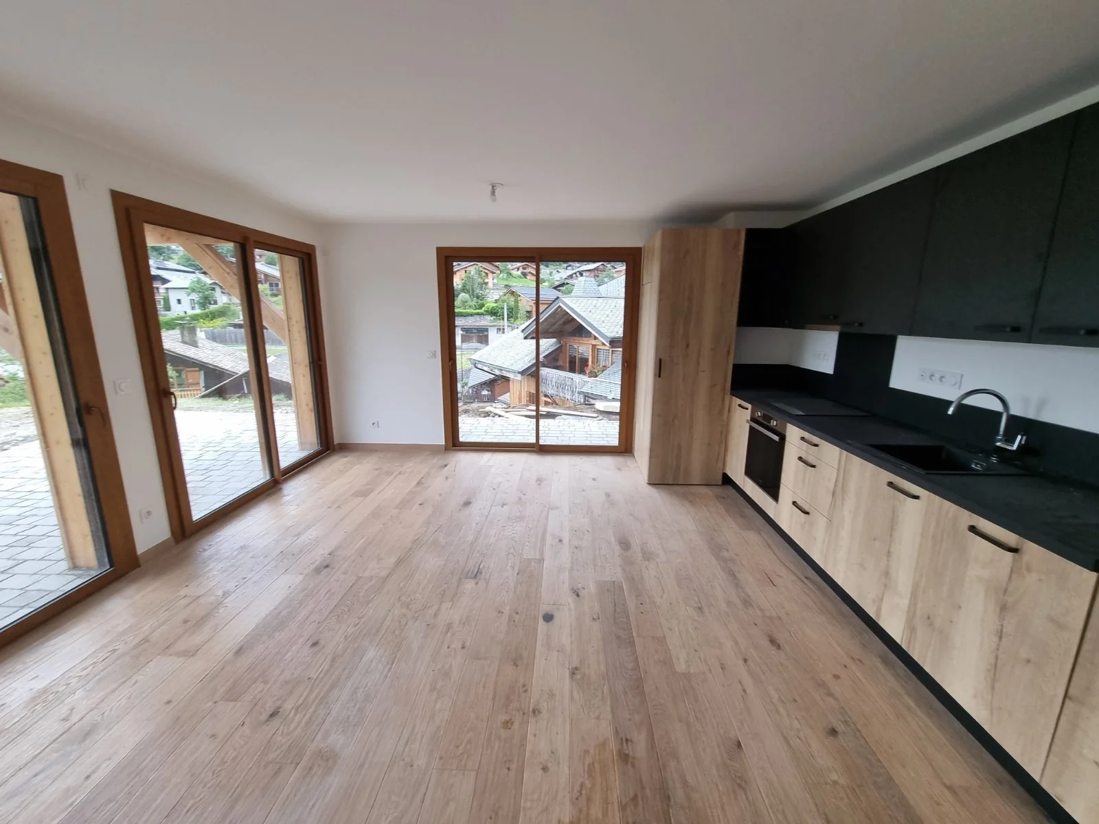 Intérieur d'une cuisine moderne avec grandes fenêtres en bois, plancher en bois clair, et armoires noires avec comptoir noir.