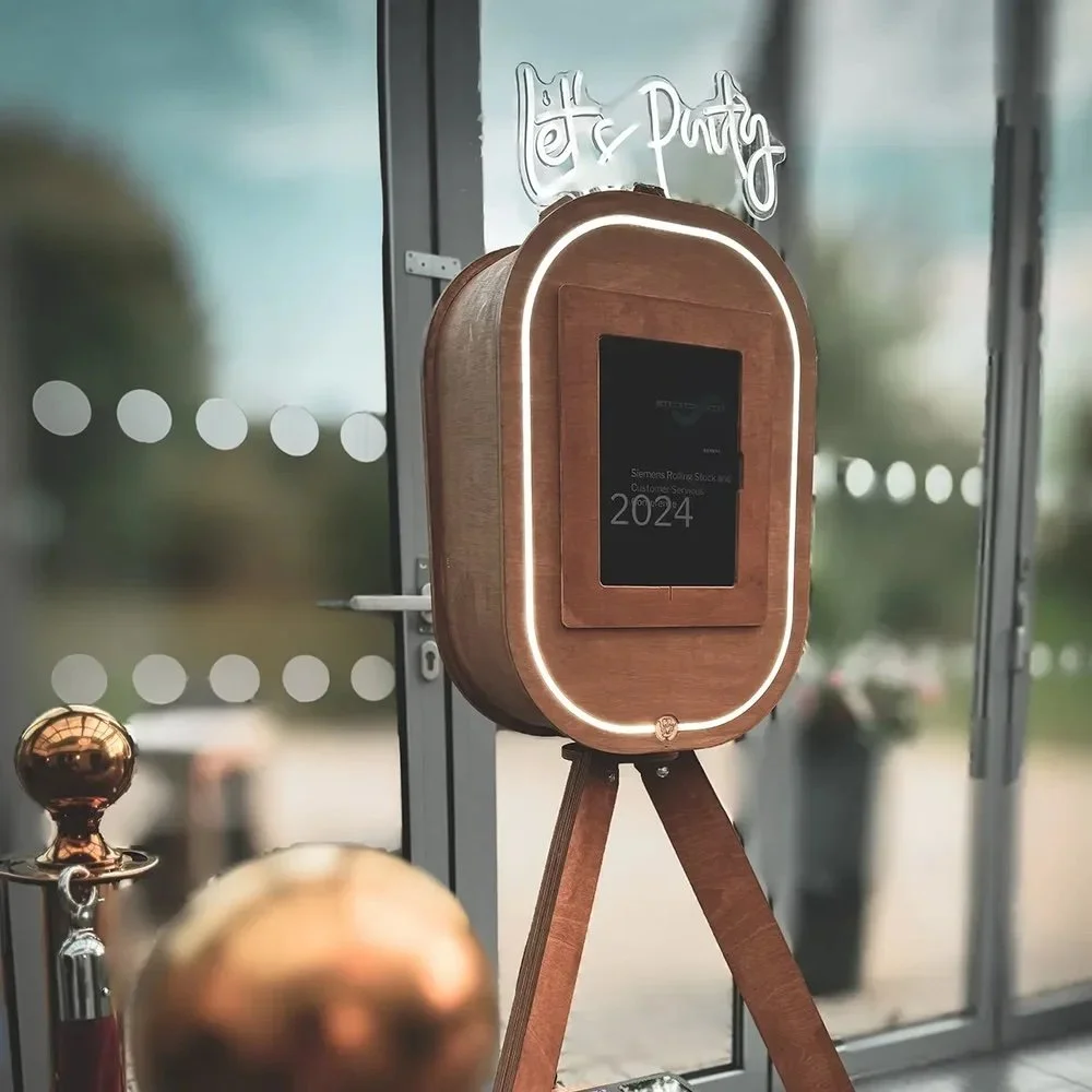 A wooden-focused digital display or kiosk positioned on a tripod stand inside or outside a building, with a neon sign that says 'Eat & Party' in the background.