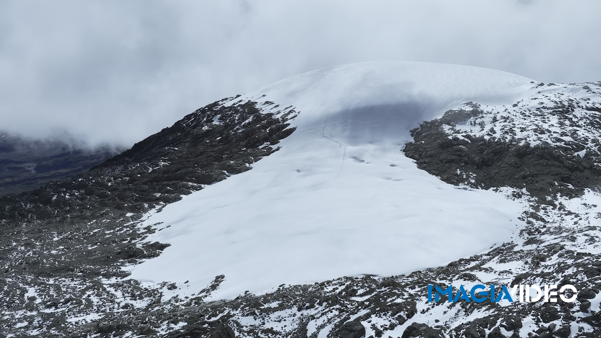 Montaña con cumbres nevadas y nubes en el cielo, caminos o huellas en la nieve en la ladera de la montaña.