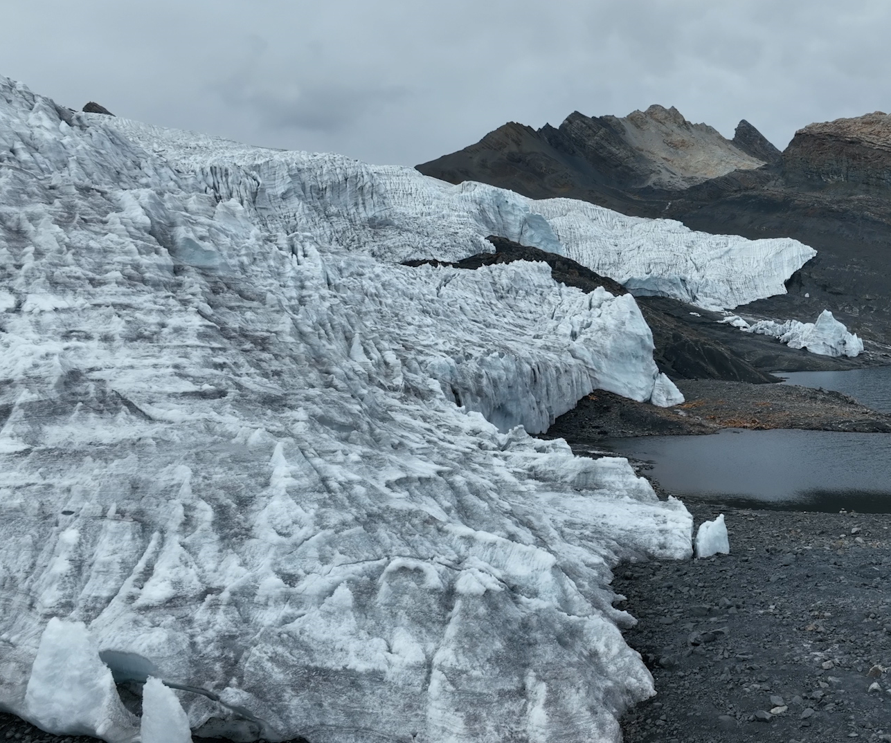 Cordillera con glaciares de hielo blanco y lagos en un paisaje montañoso nublado.