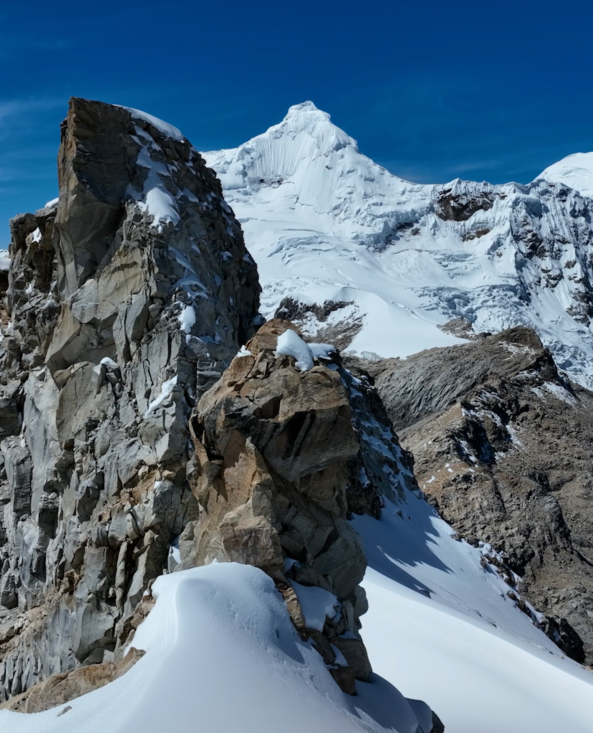 Montañas cubiertas de nieve con rocas, nevada y un cielo azul.
