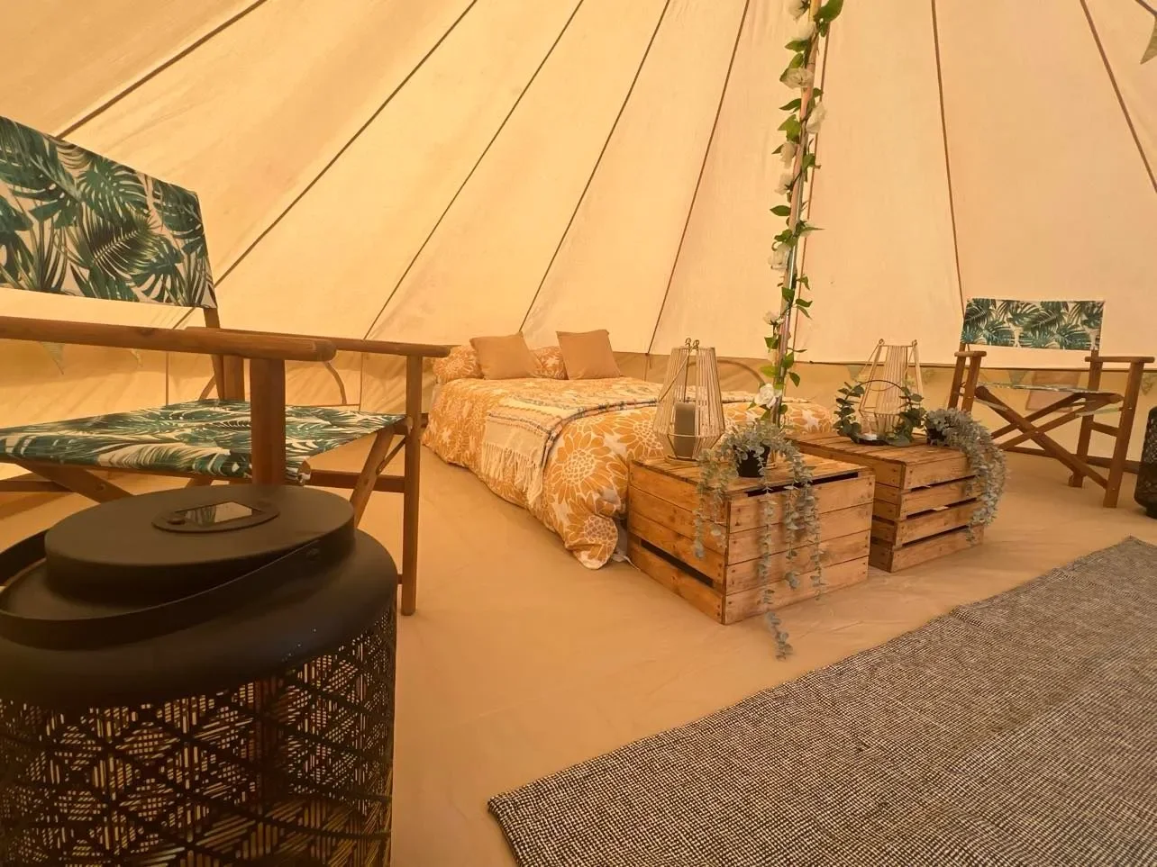 Inside a cozy, decorated tent with a bed, wooden crates as coffee tables, patterned chairs, lanterns, and floral decorations.