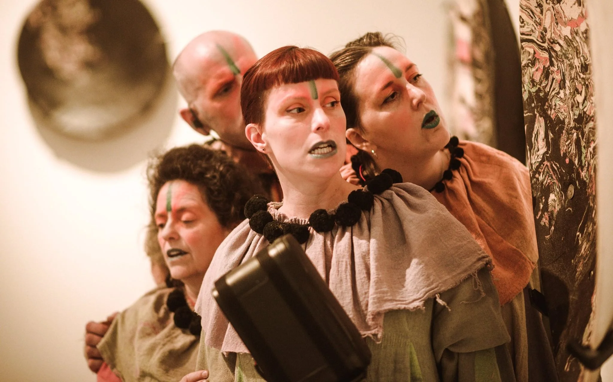 A group of four white people in hessian costumes with green face markings are singing.
