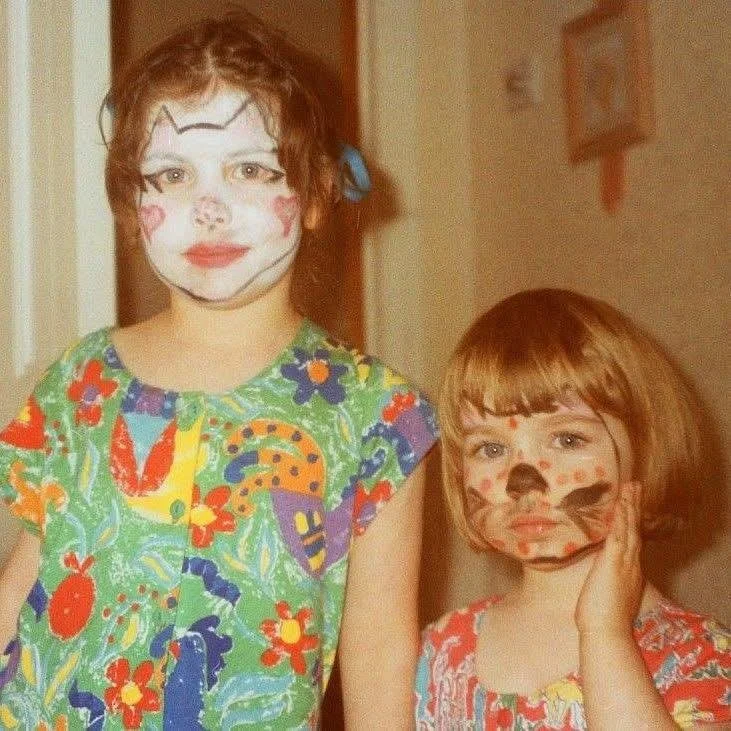 Old photo from the 1990s shows two young white girls with colourful face paint and clothes, standing indoors.
