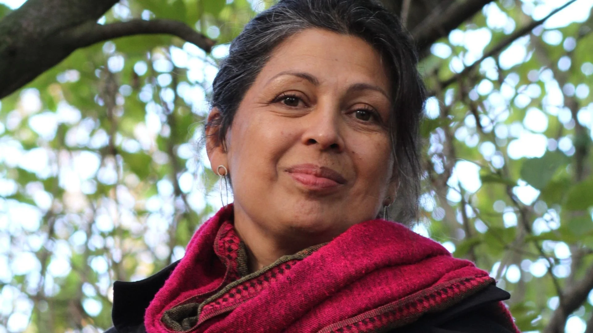 A Brown woman wearing a red scarf smiles at the camera.