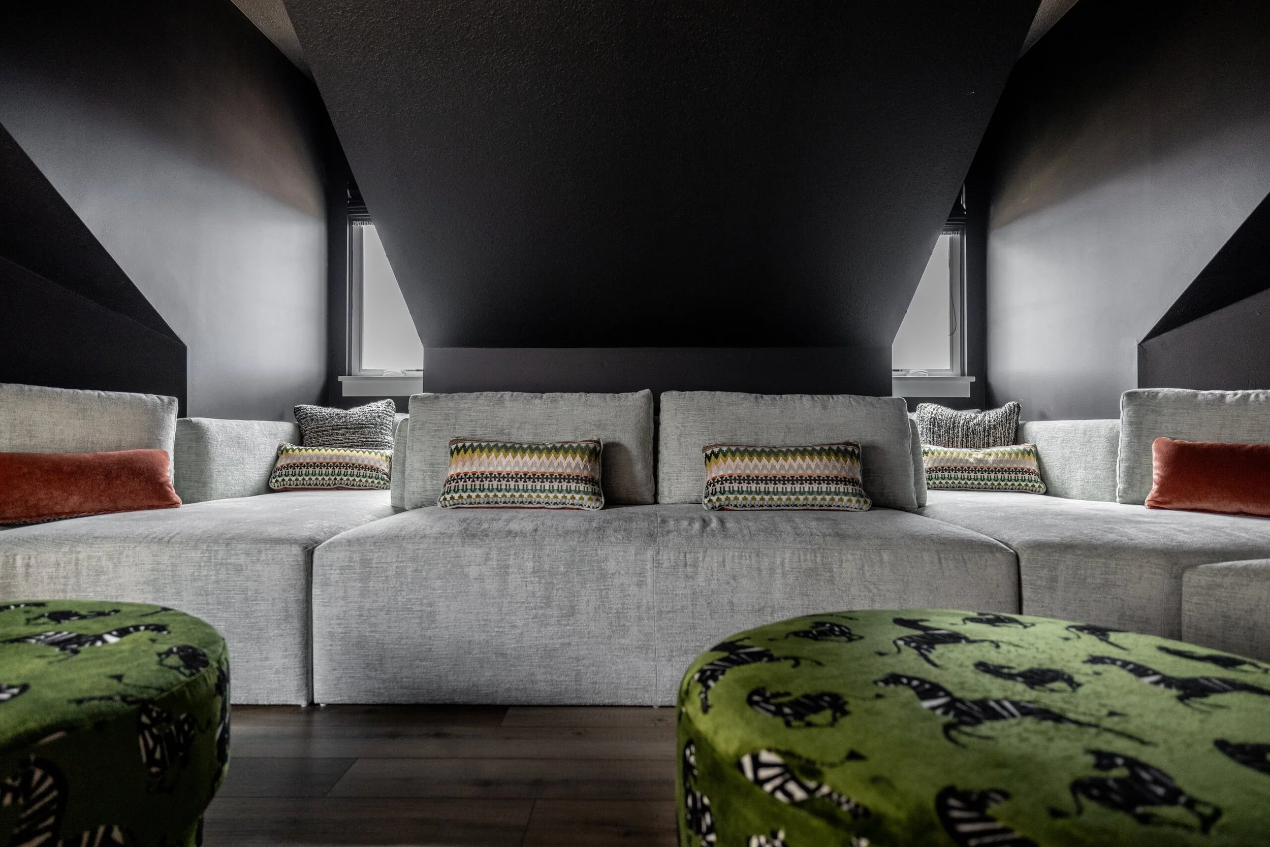 Bonus room hideaway with a dark sloped ceiling, deep gray sectional and green patterned ottomans