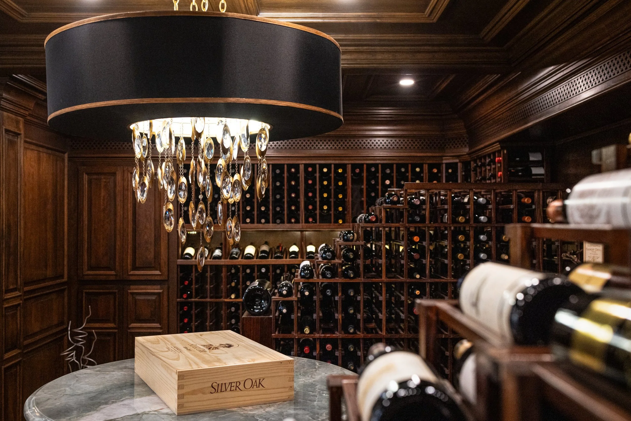 Luxury wine cellar with dark wood paneling, floor to ceiling wine racks and a black drum chandelier with crystals