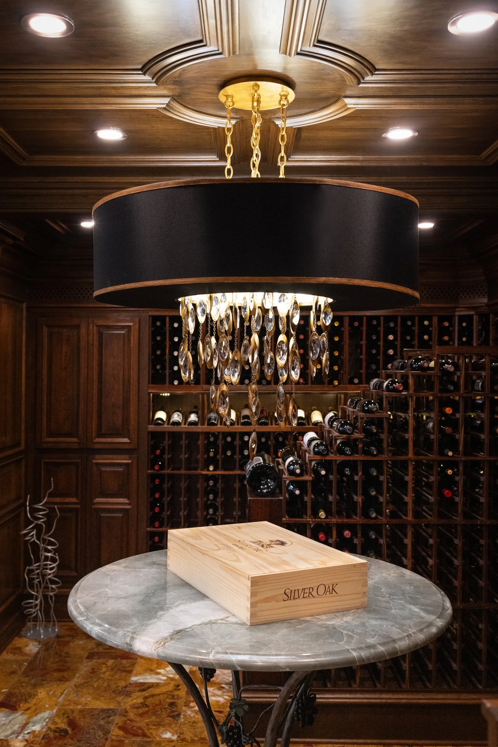 Round stone topped tasting table under a crystal chandelier in a wood paneled wine cellar