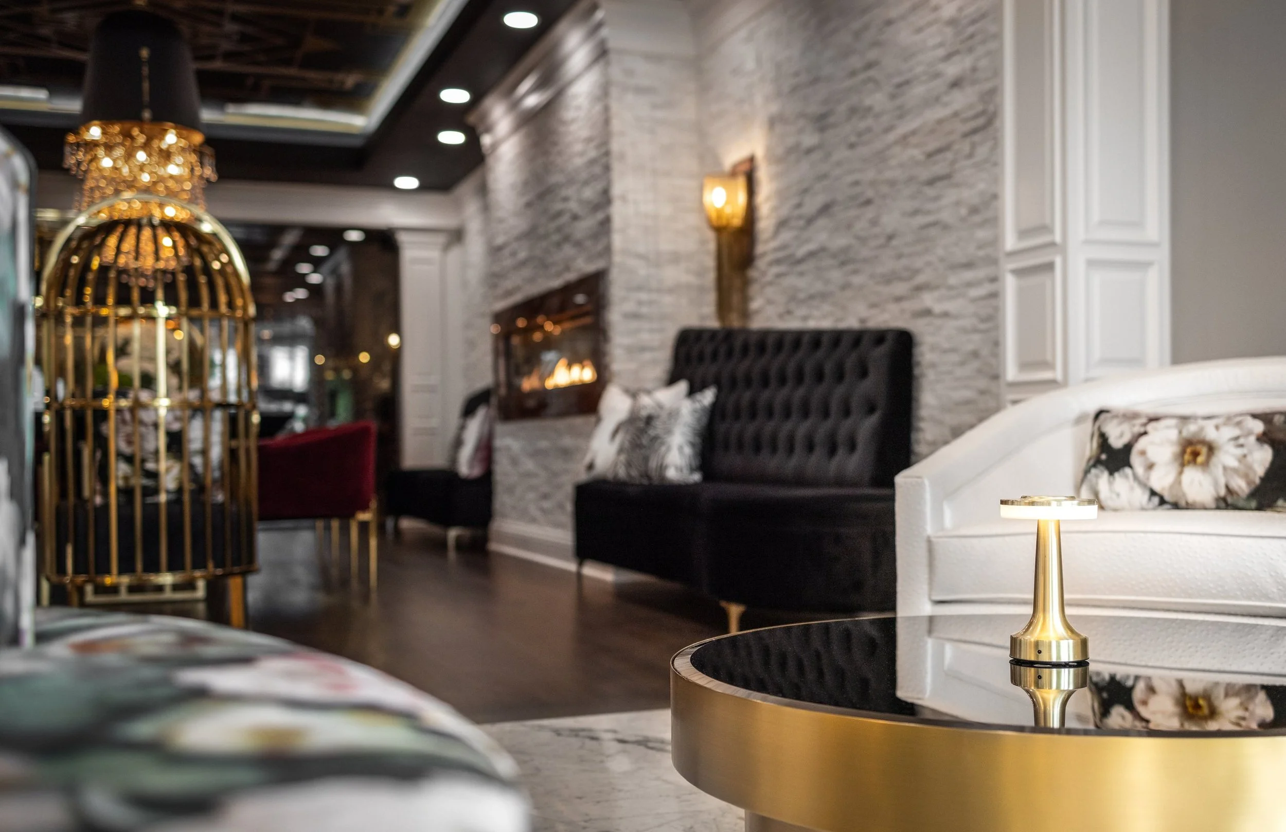 Gold birdcage chair beside a black velvet banquette and a linear fireplace in a lower level lounge