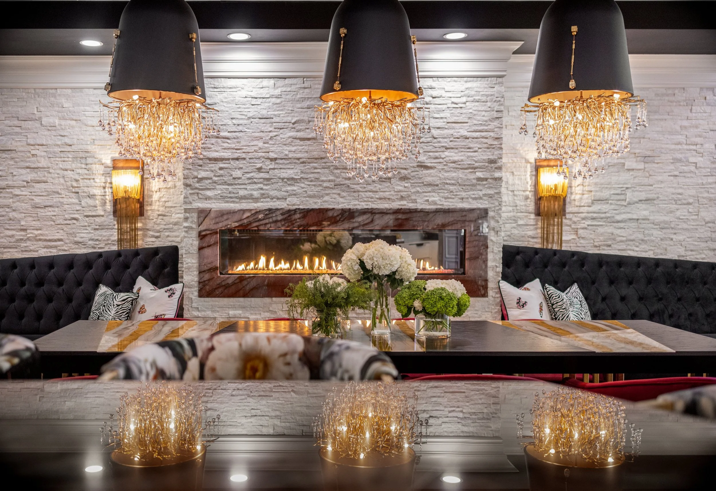 Linear fireplace in a white stacked stone wall with tufted black velvet banquettes and brass sconces