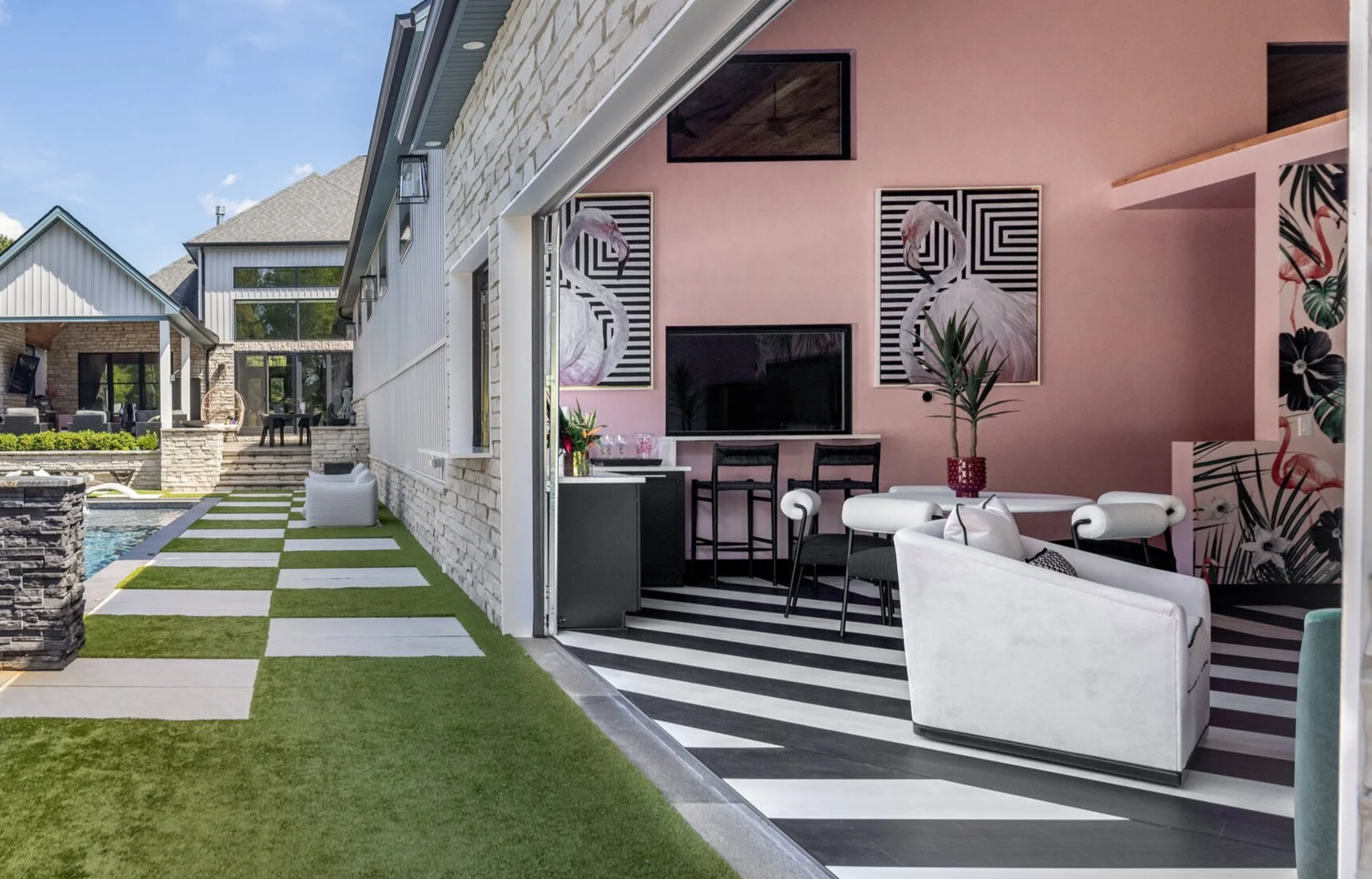 Checkerboard stone pavers leading past the pool to a pink cabana lounge with black and white striped floors