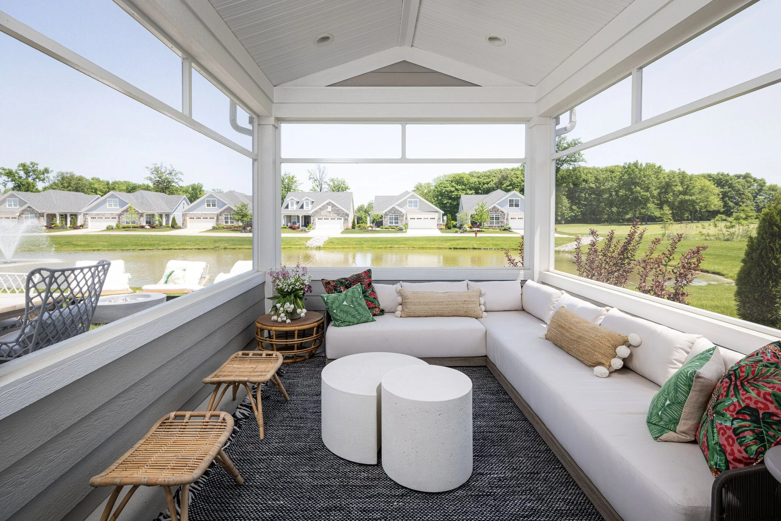 Screened porch lounge with a white sectional, rattan stools and a view of the lake