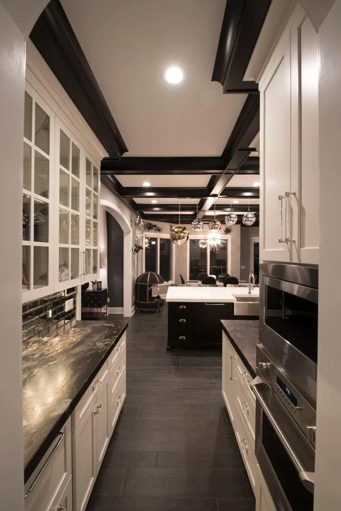 Butler's pantry with glass-front white cabinets, black stone counters and a coffered ceiling leading from the kitchen to the dining room