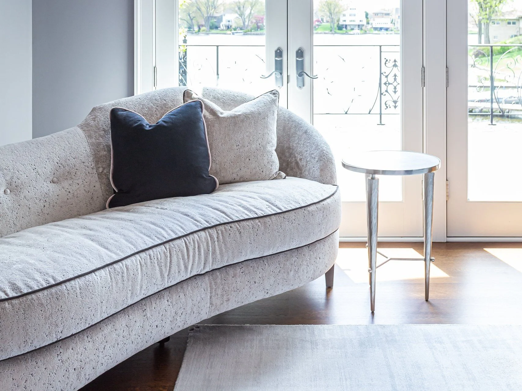 Curved upholstered settee and small side table beside French doors in a primary bedroom