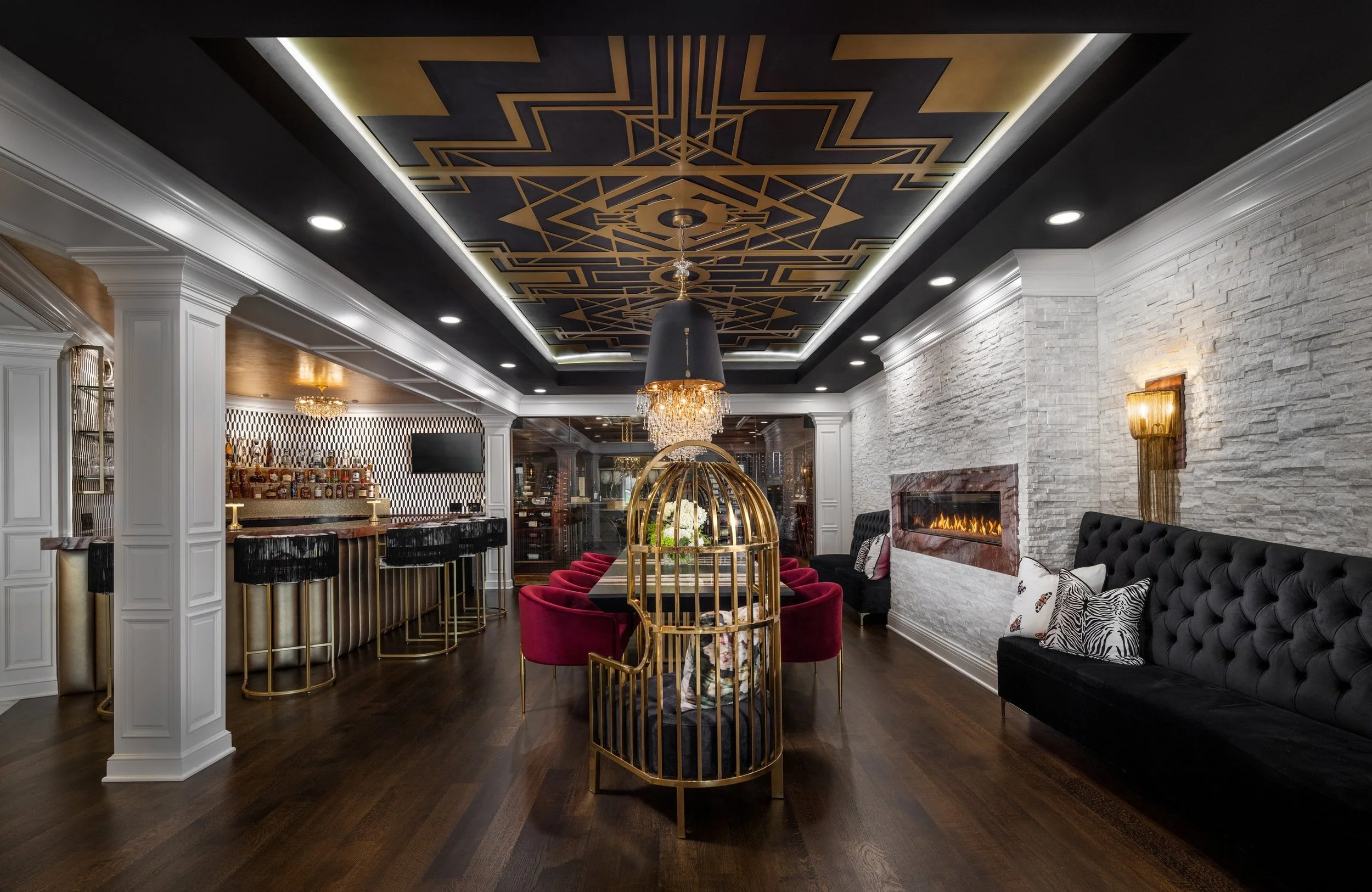Long lower level with a cocktail bar, tasting table, glass wine cellar and fireplace under an art deco ceiling