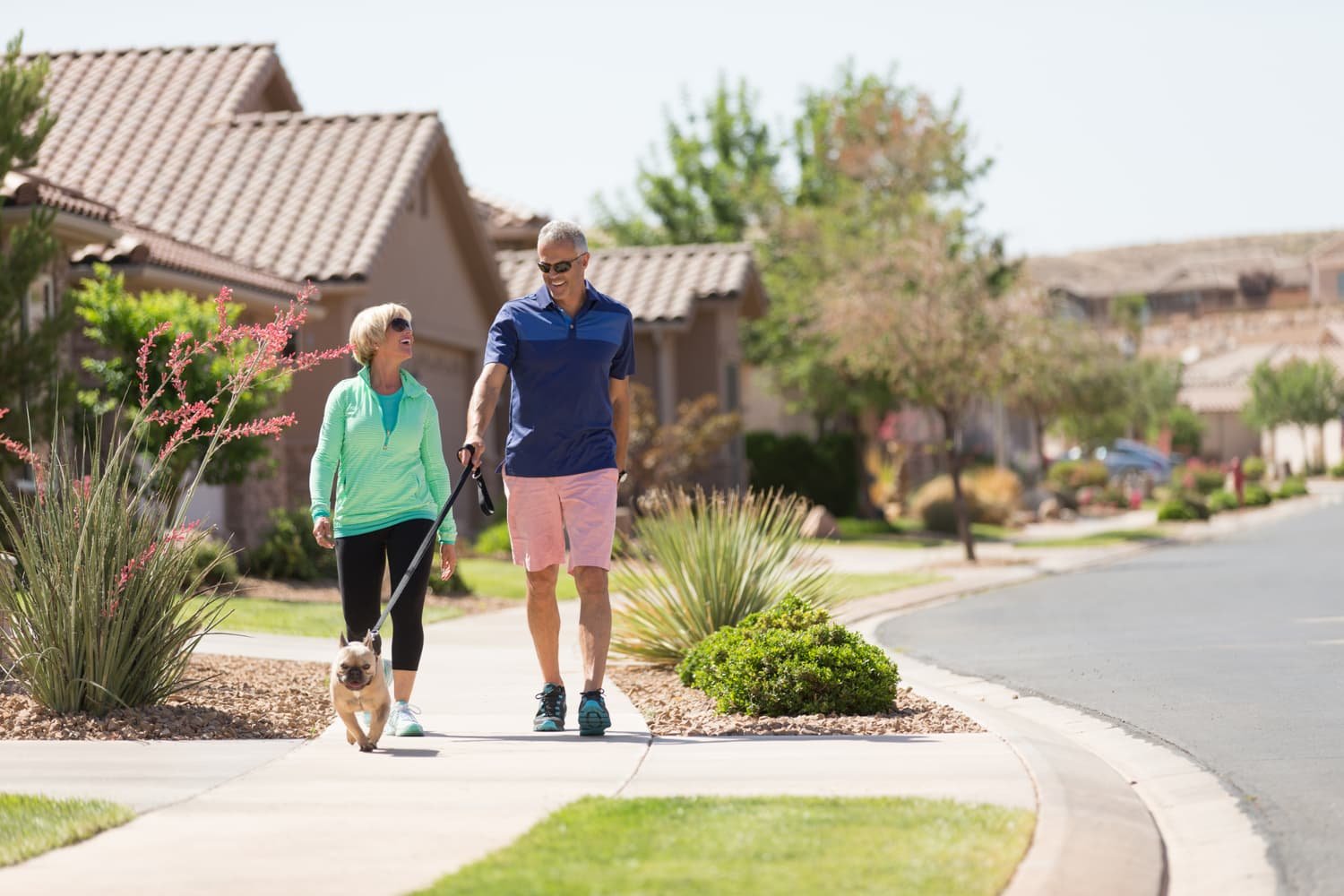 Couple walking their dog through a sunny Southern Utah neighborhood — the kind of second-home community served by KeyBird Home Watch & Concierge in St. George