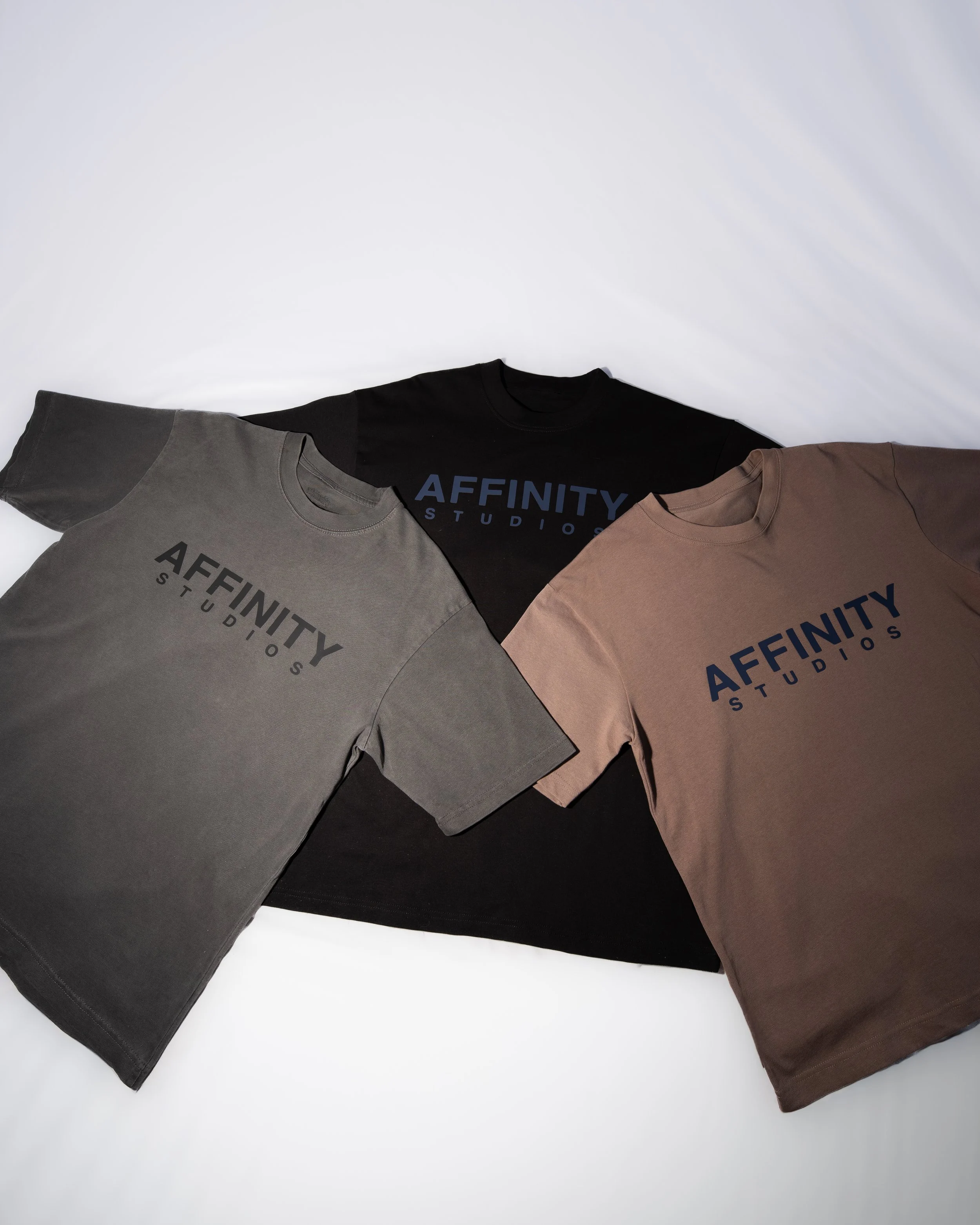 Three T-shirts laid out flat on a white surface, each with 'AFFINITY STUDIOS' printed on the front in large letters