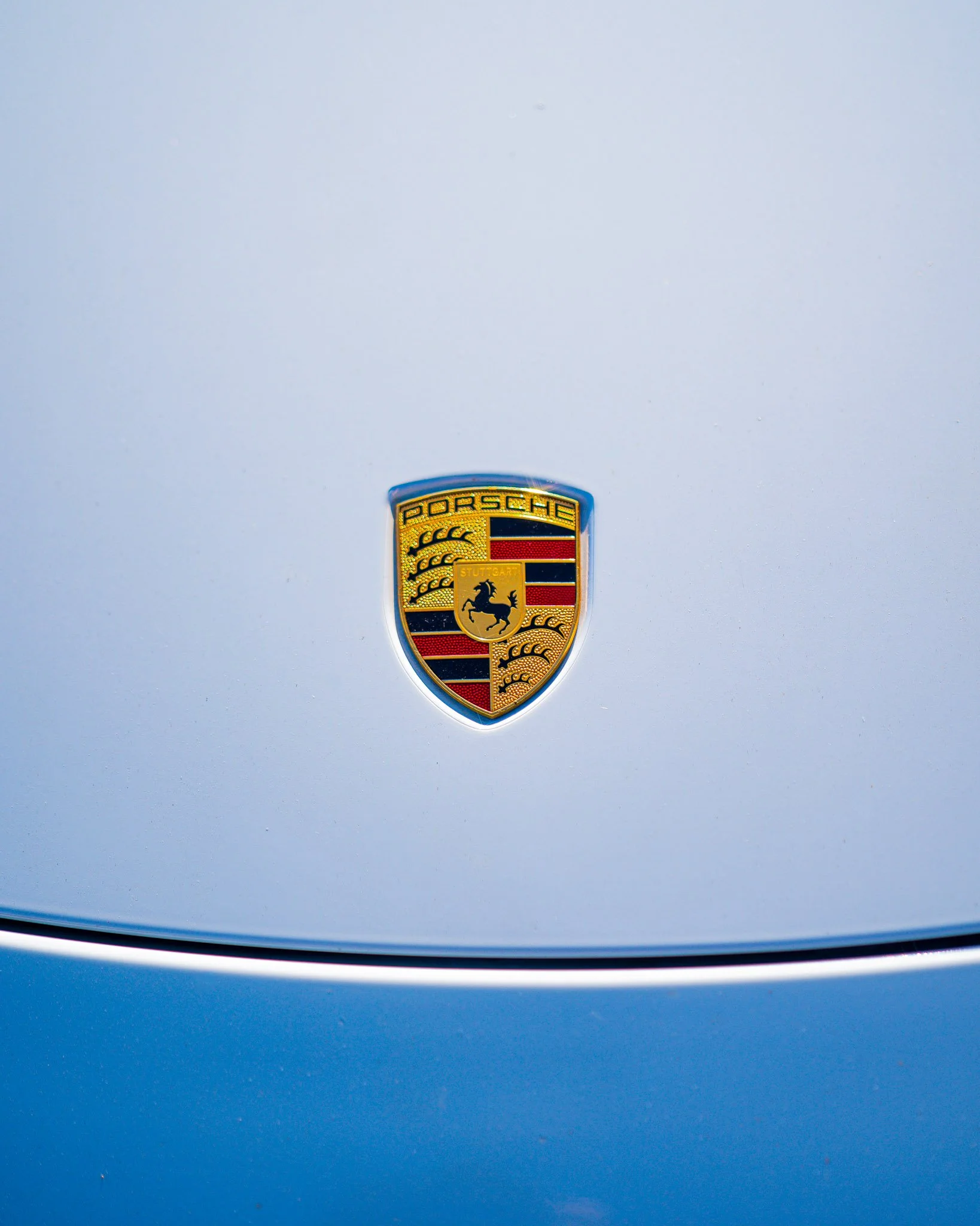 Close-up of a silver car hood featuring the Porsche emblem in the center.