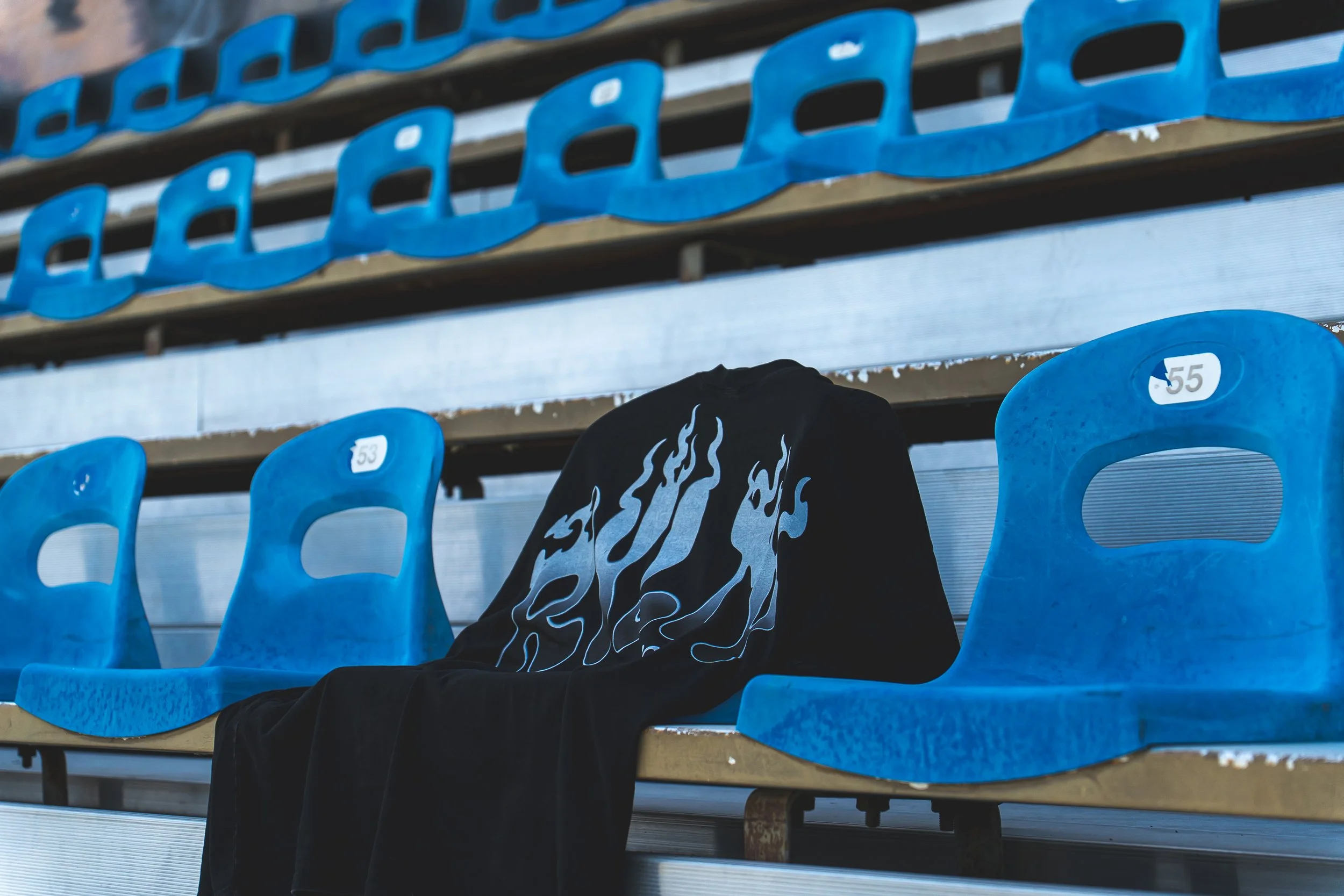 Empty blue stadium seats with one seat holding a black jacket with white flame pattern.